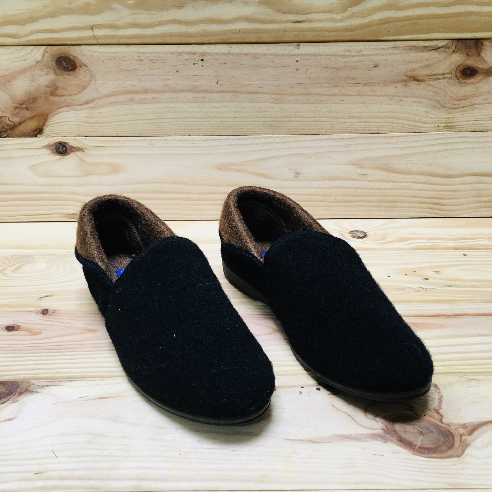 Chinelos pretos de tecido com interior castanho sobre superfície de madeira clara
