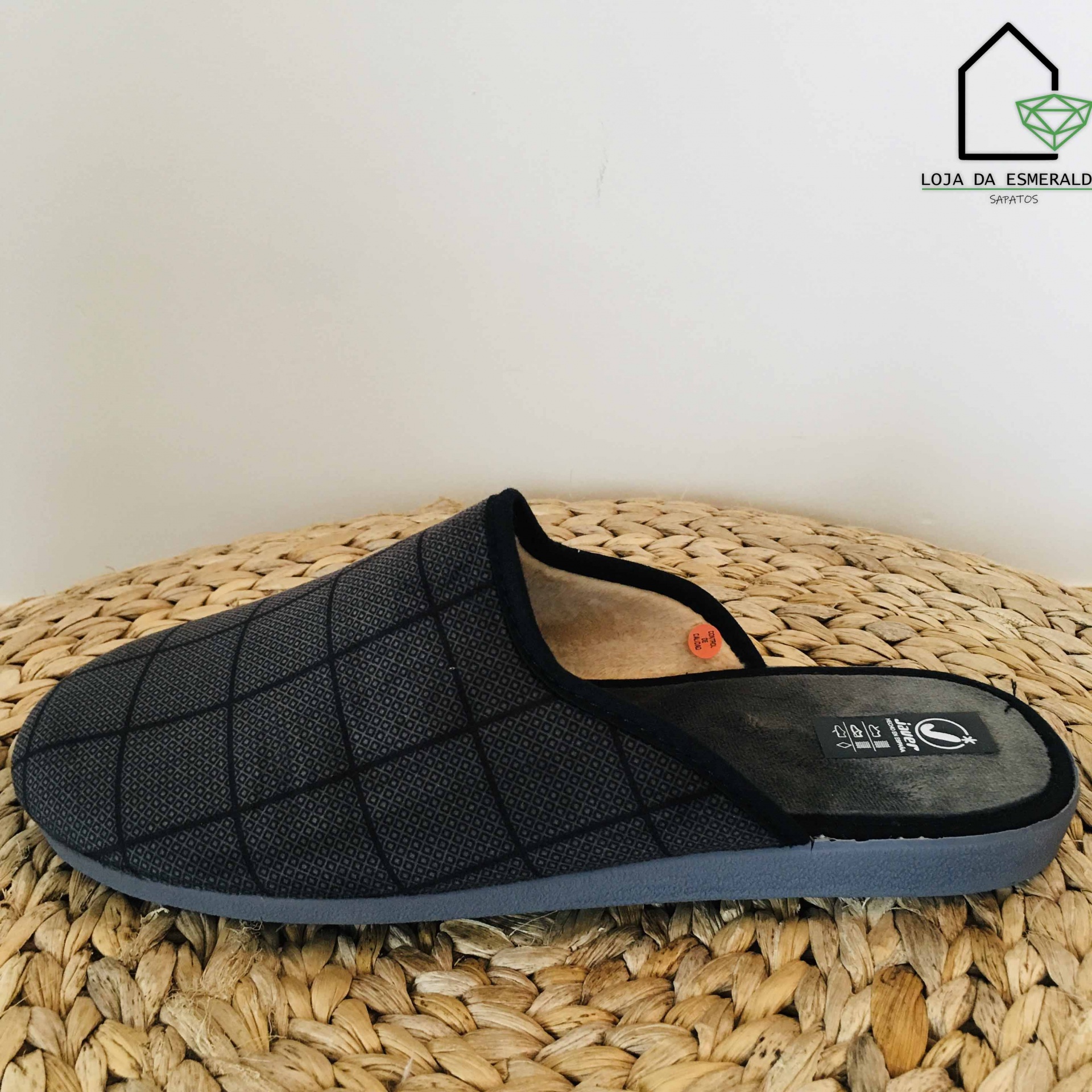 Chinelo mule preto com padrão quadriculado e solado cinzento sobre superfície de palha