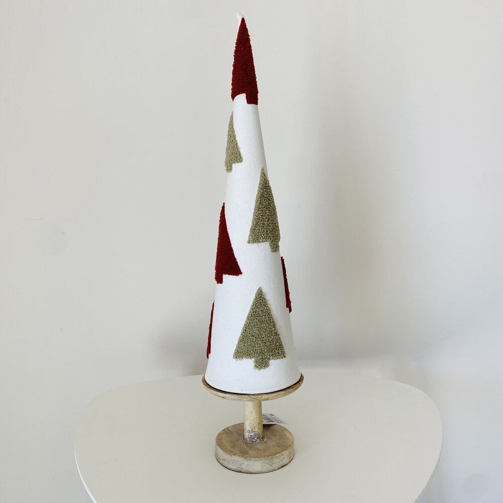 Árvore de Natal decorativa em tecido branco com padrões de árvores verdes e vermelhas, com base de madeira sobre mesa branca.