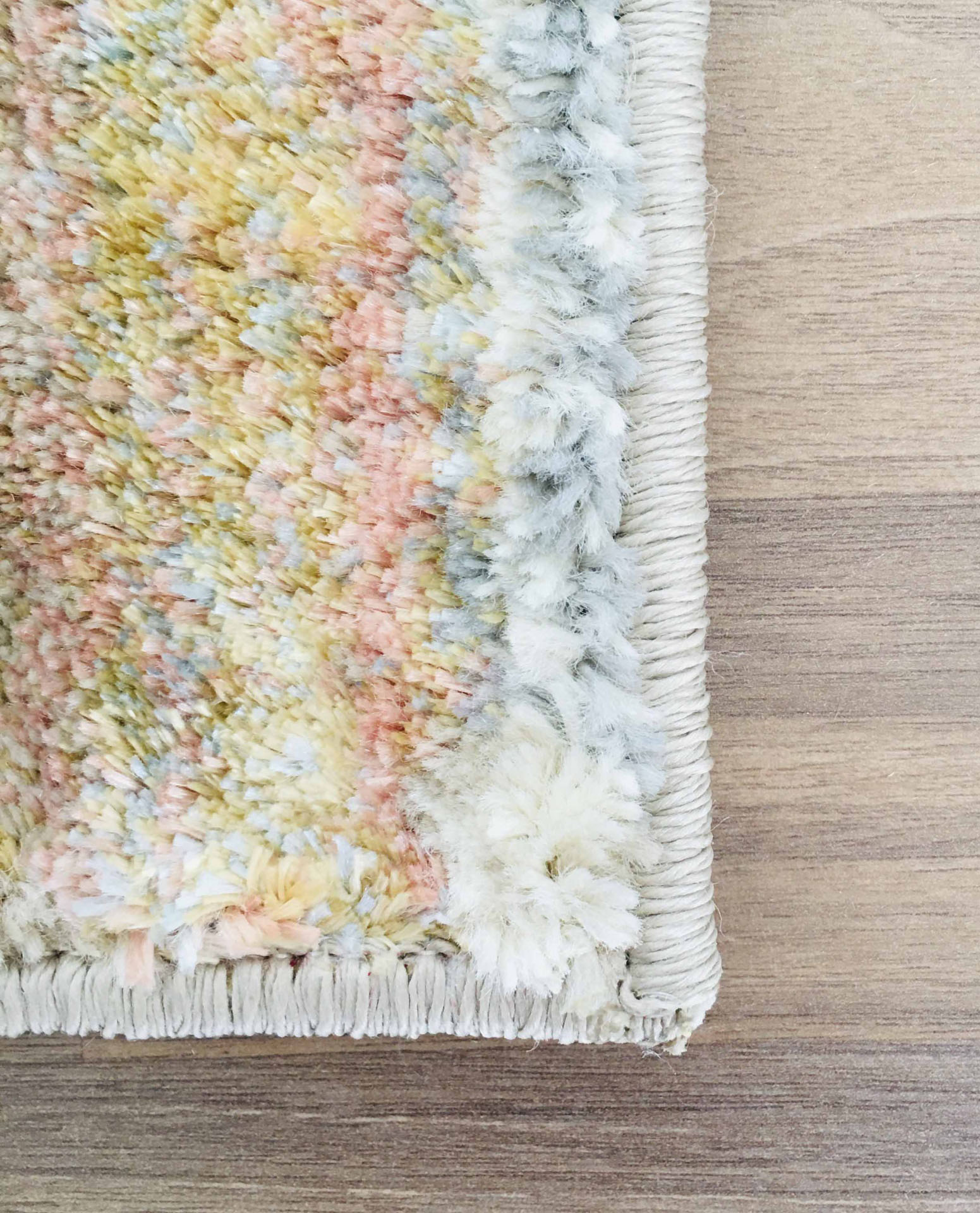 Canto de tapete felpudo multicolor pastel sobre piso de madeira clara