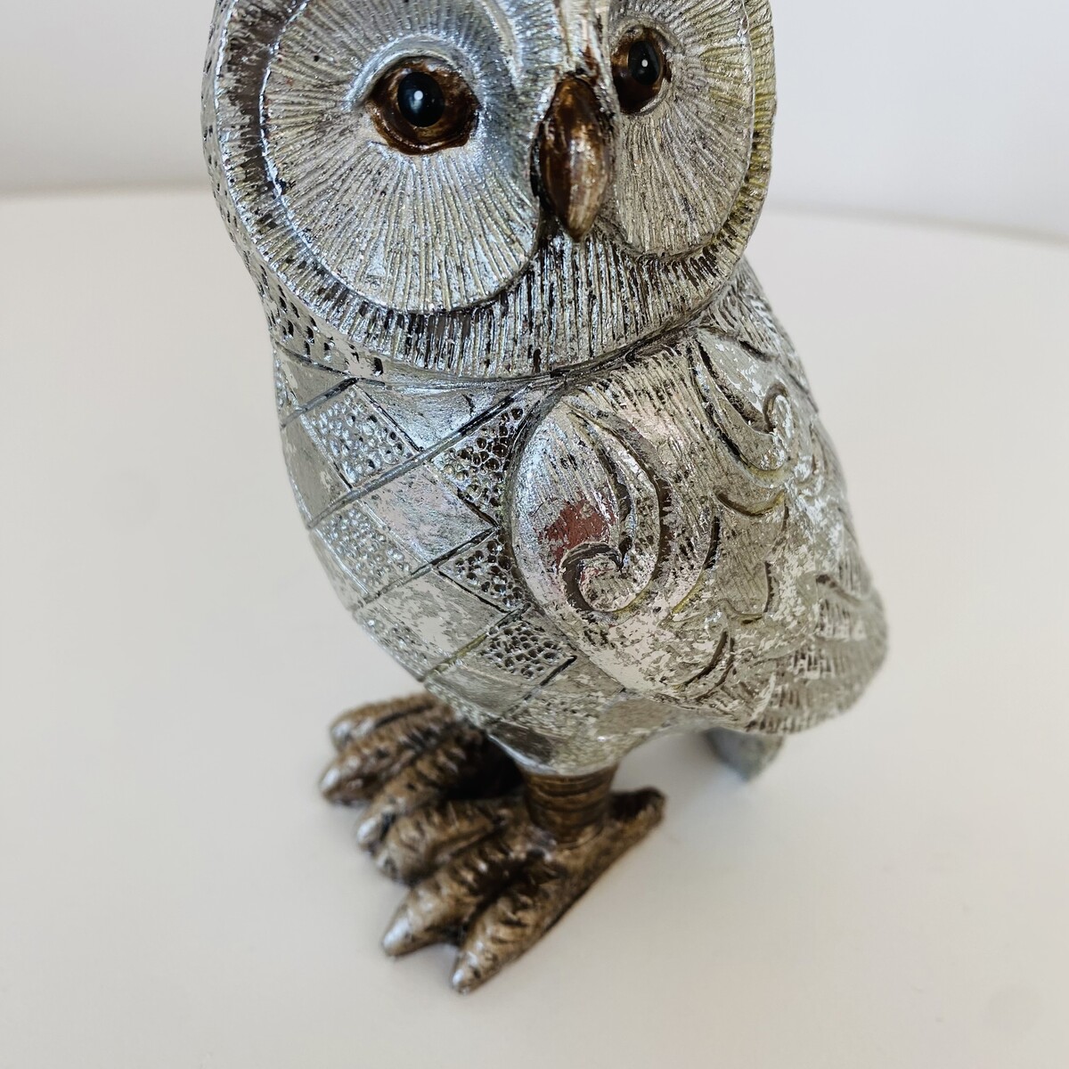 Estátua de coruja metálica prateada com detalhes gravados