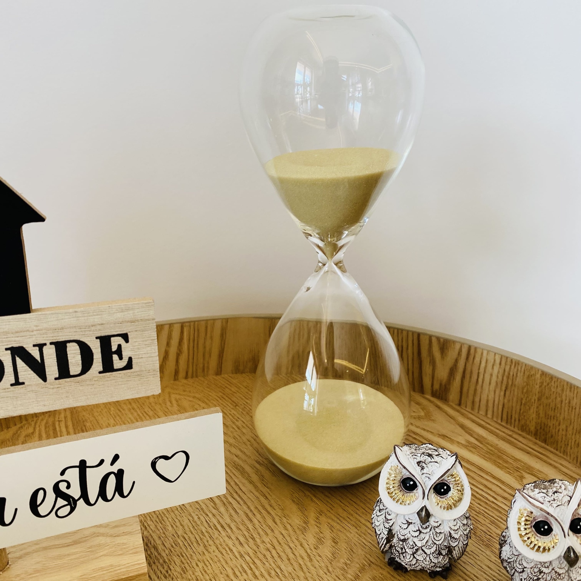Ampulheta de vidro com areia amarela entre objetos decorativos em madeira e esculturas de coruja
