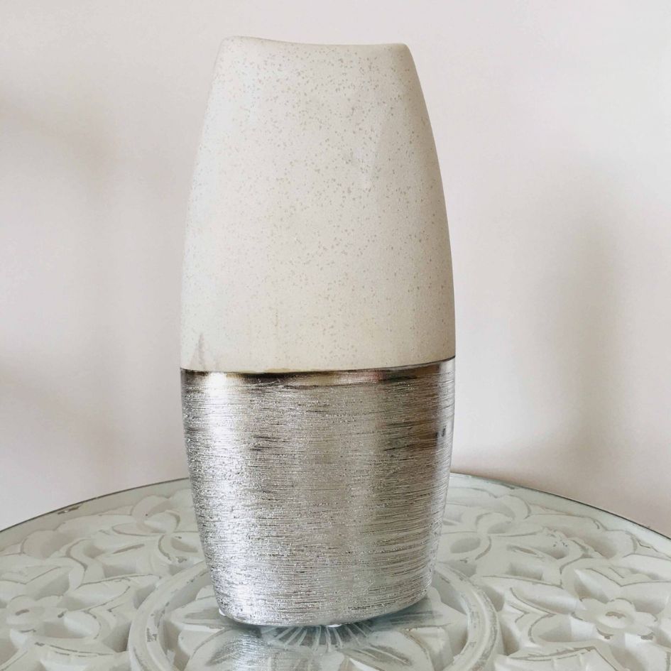 Vaso decorativo bege e prateado com textura sobre mesa de vidro