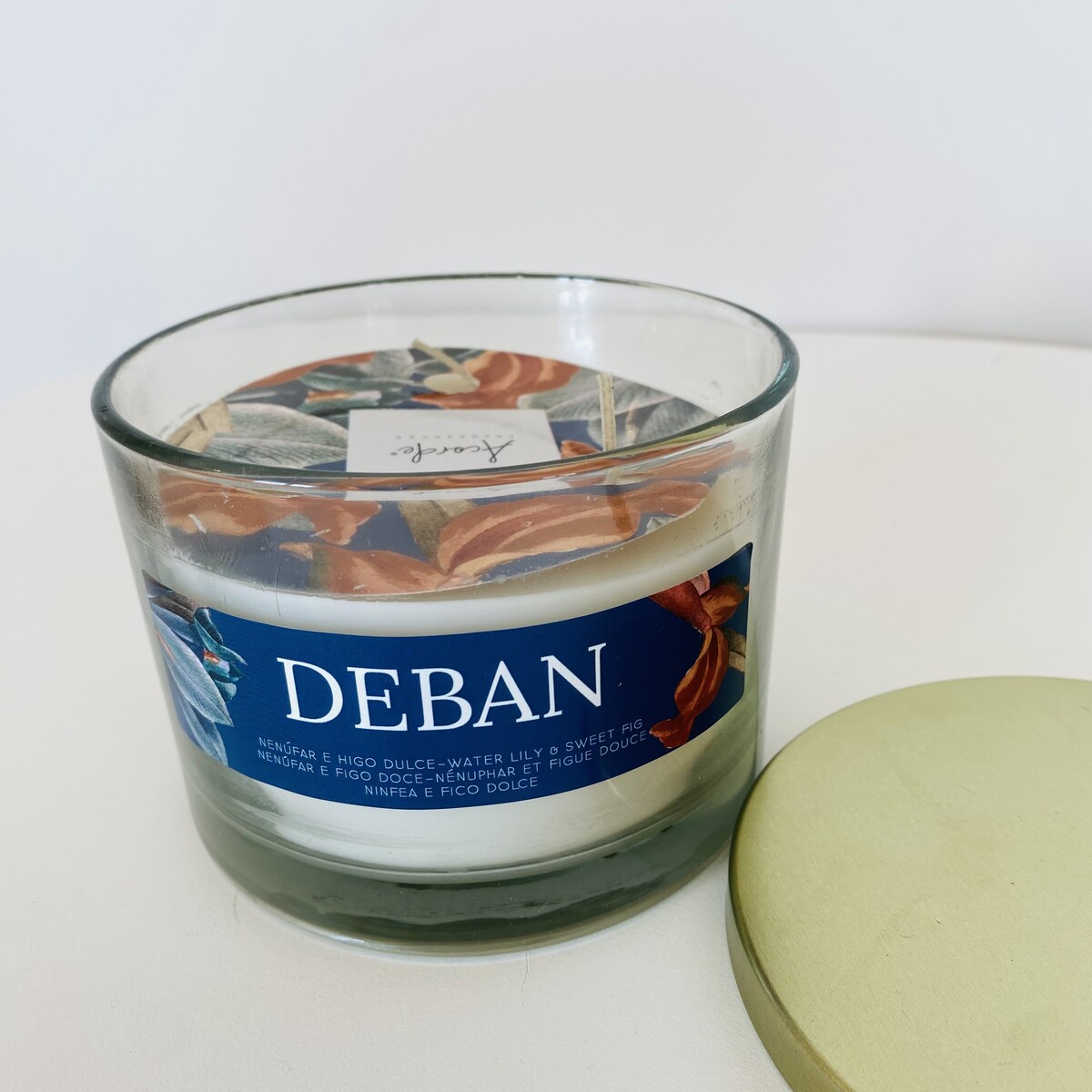 vela em vidro com etiqueta azul e tampa dourada ao lado