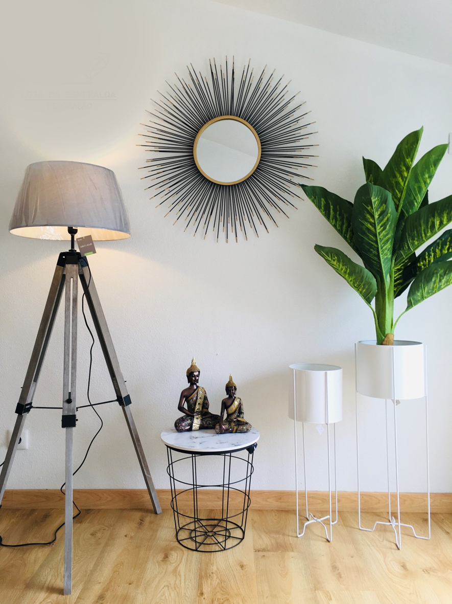 Luminária de tripé, mesa redonda com esculturas, suportes para plantas brancos, planta verde e espelho redondo decorativo