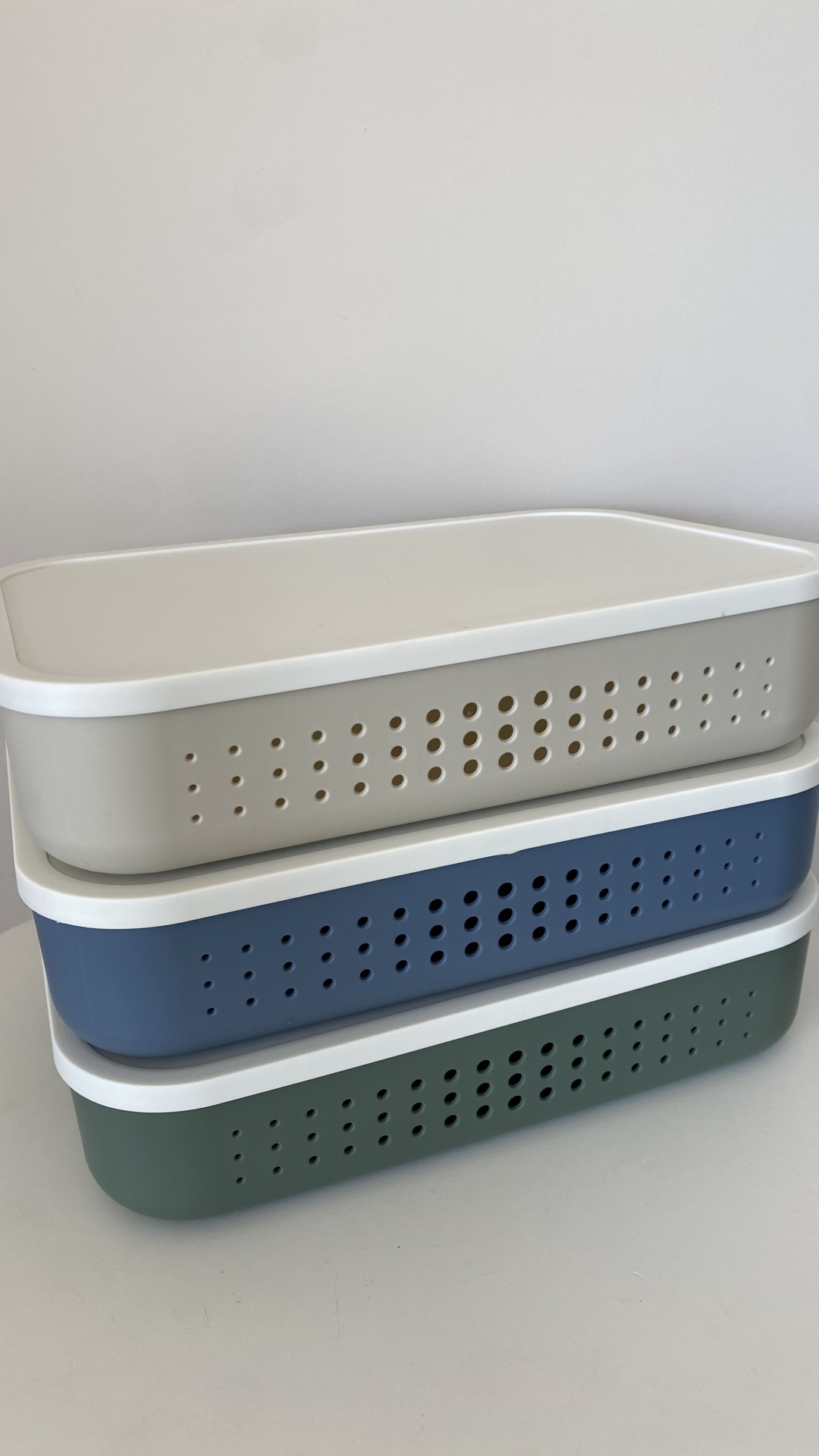 Três caixas plásticas empilhadas com tampas brancas e lados perfurados em diferentes cores.