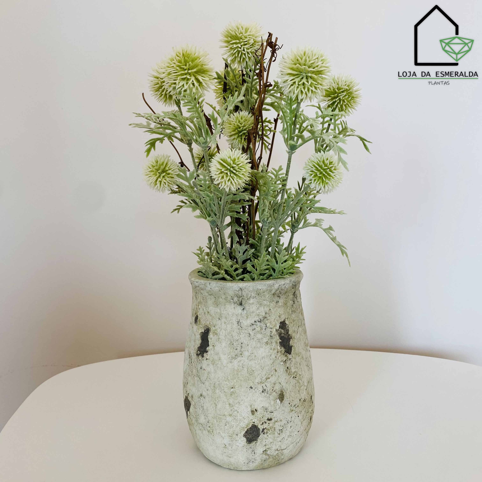 Vaso cinzento com flores artificiais verdes e folhas em mesa branca