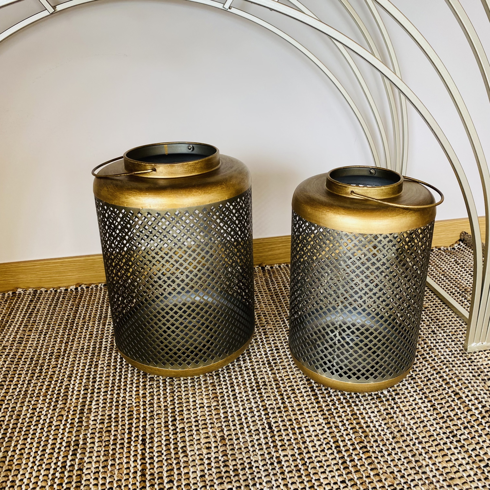 Duas lanternas metálicas douradas em padrão de grelha, sobre tapete bege texturizado