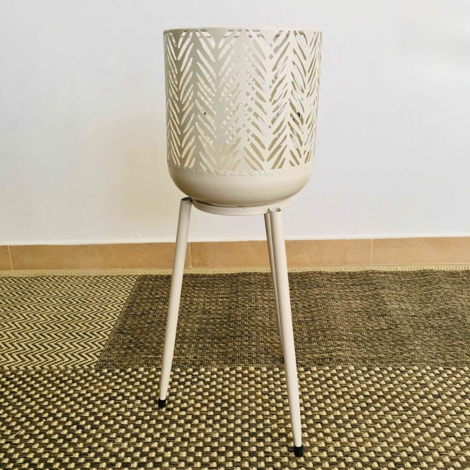 Suporte de plantas metálico creme com padrão em folhas em fase de tripé sobre tapete padrão geométrico