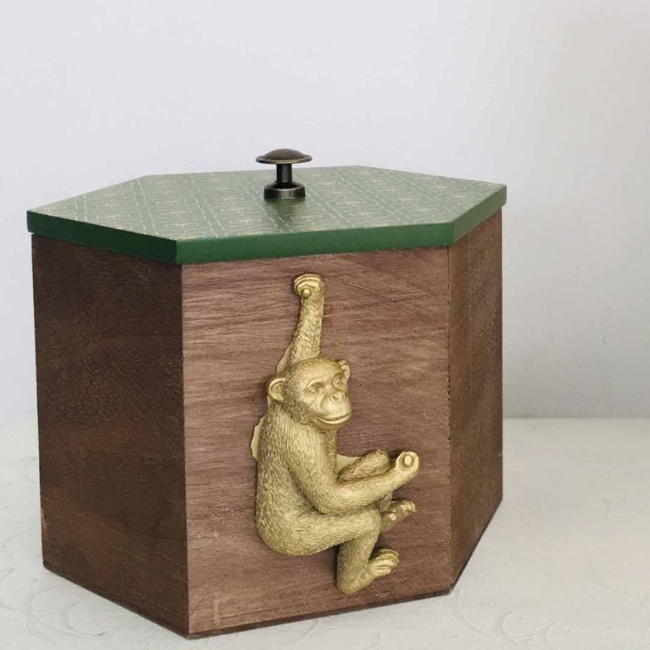 Caixa hexagonal de madeira com tampa verde e macaco dourado pendurado na lateral