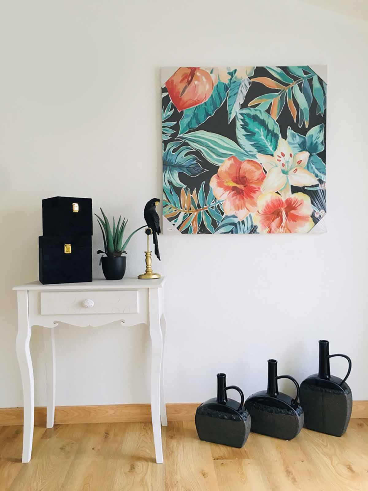 Mesa branca com objetos pretos e quadro floral colorido na parede