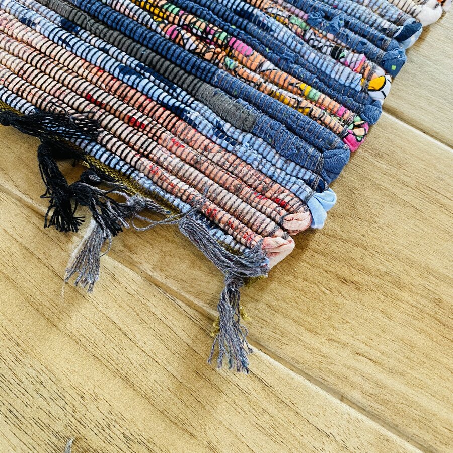 Tapete tecido colorido com franjas sobre chão de madeira clara