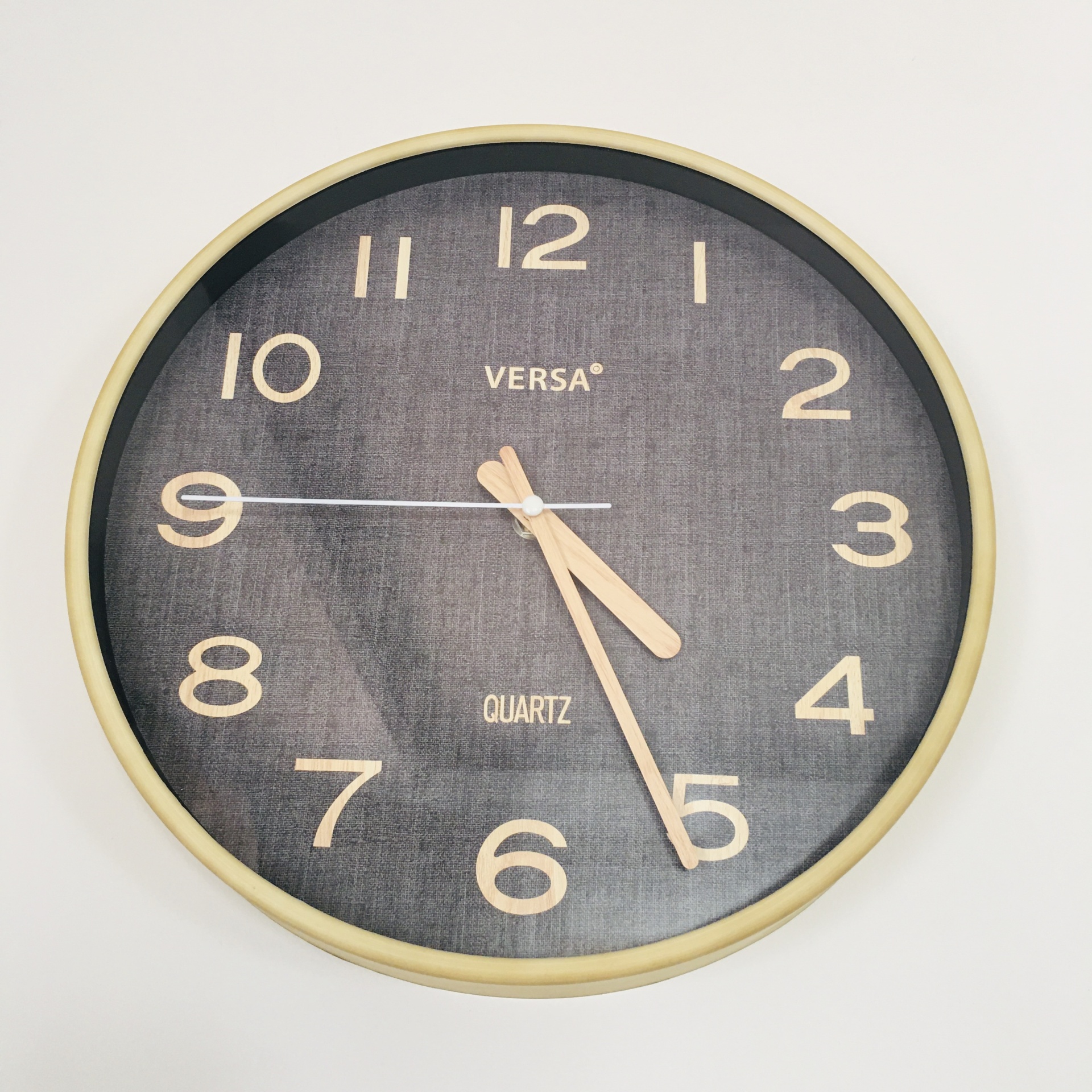 Relógio de parede redondo com fundo cinzento escuro e números e ponteiros bege