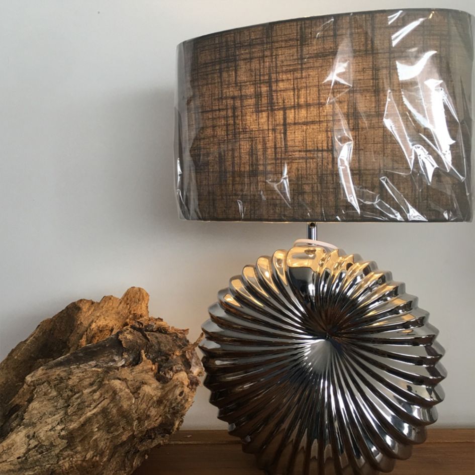 Candeeiro de mesa com base prateada e cúpula castanha texturizada numa mesa em madeira