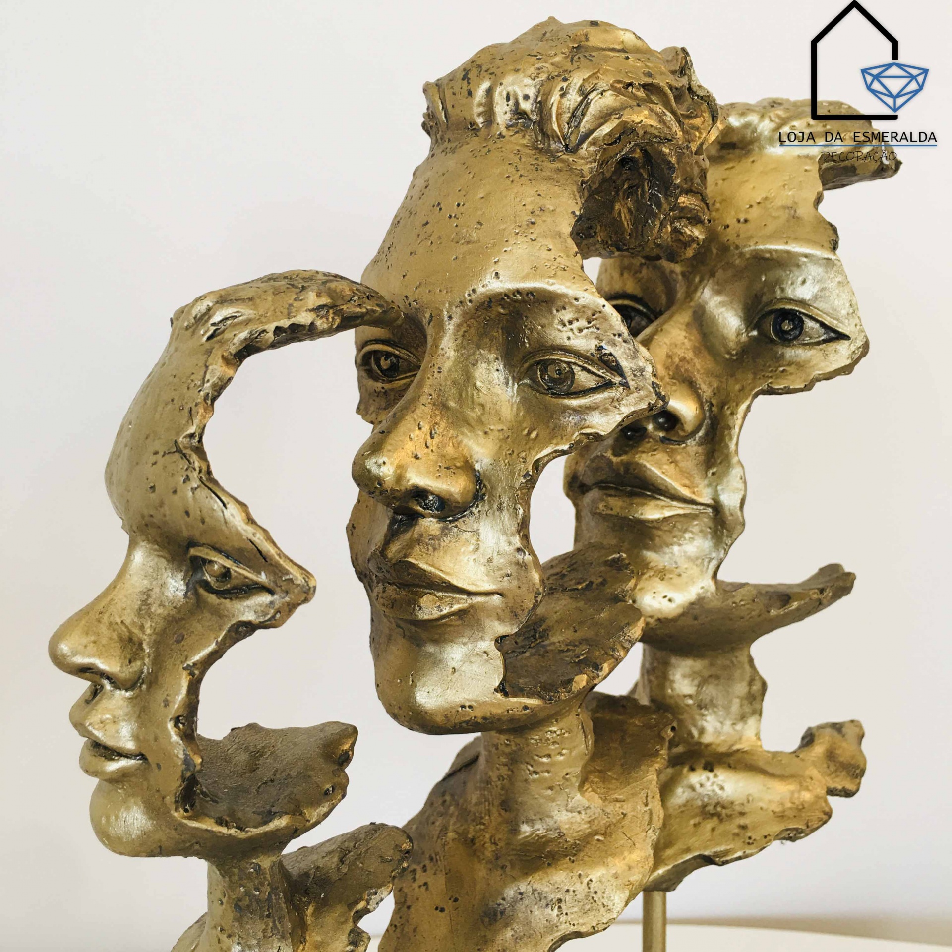 Escultura dourada com três rostos humanos interligados e textura rugosa