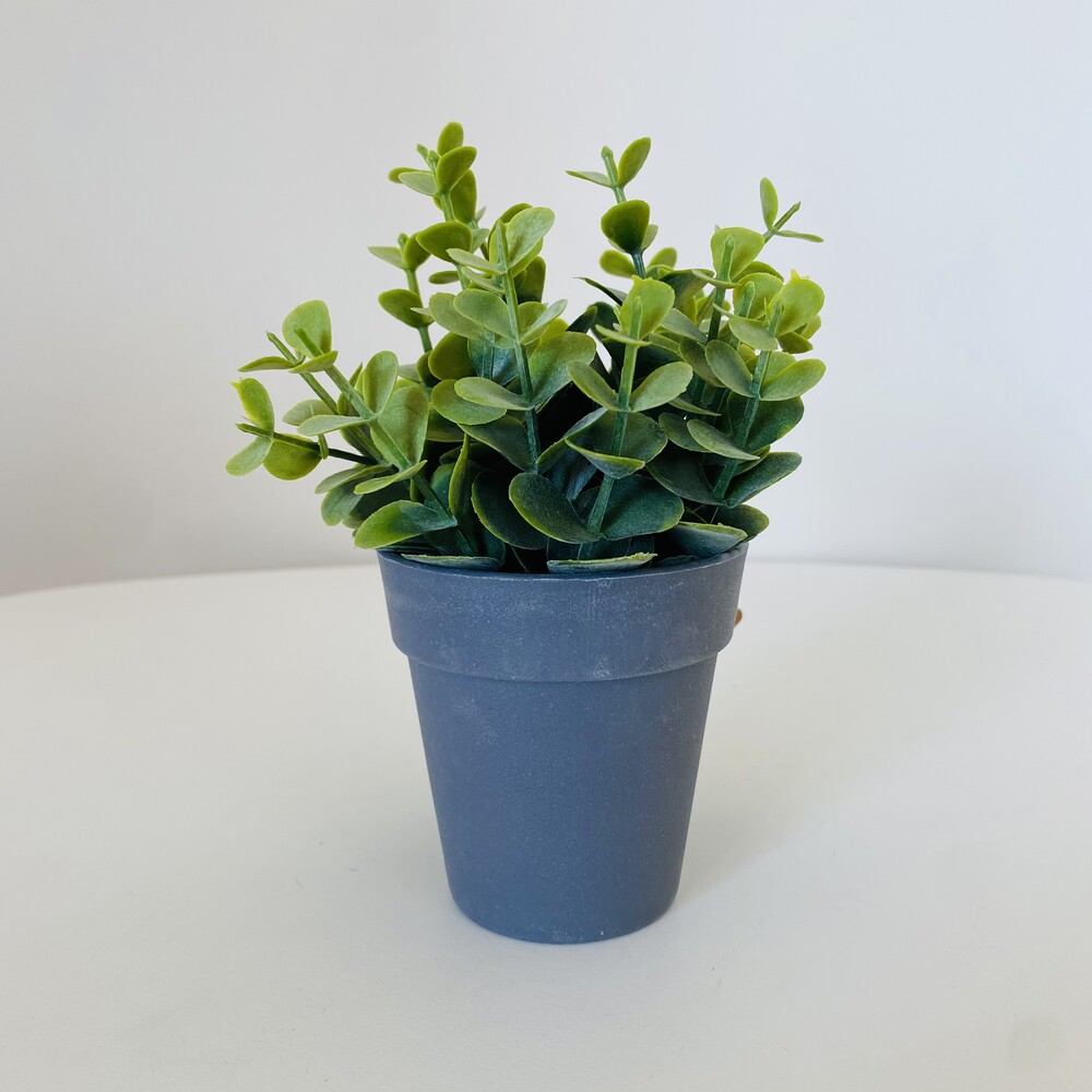 Vaso azul escuro com planta artificial verde em superfície branca