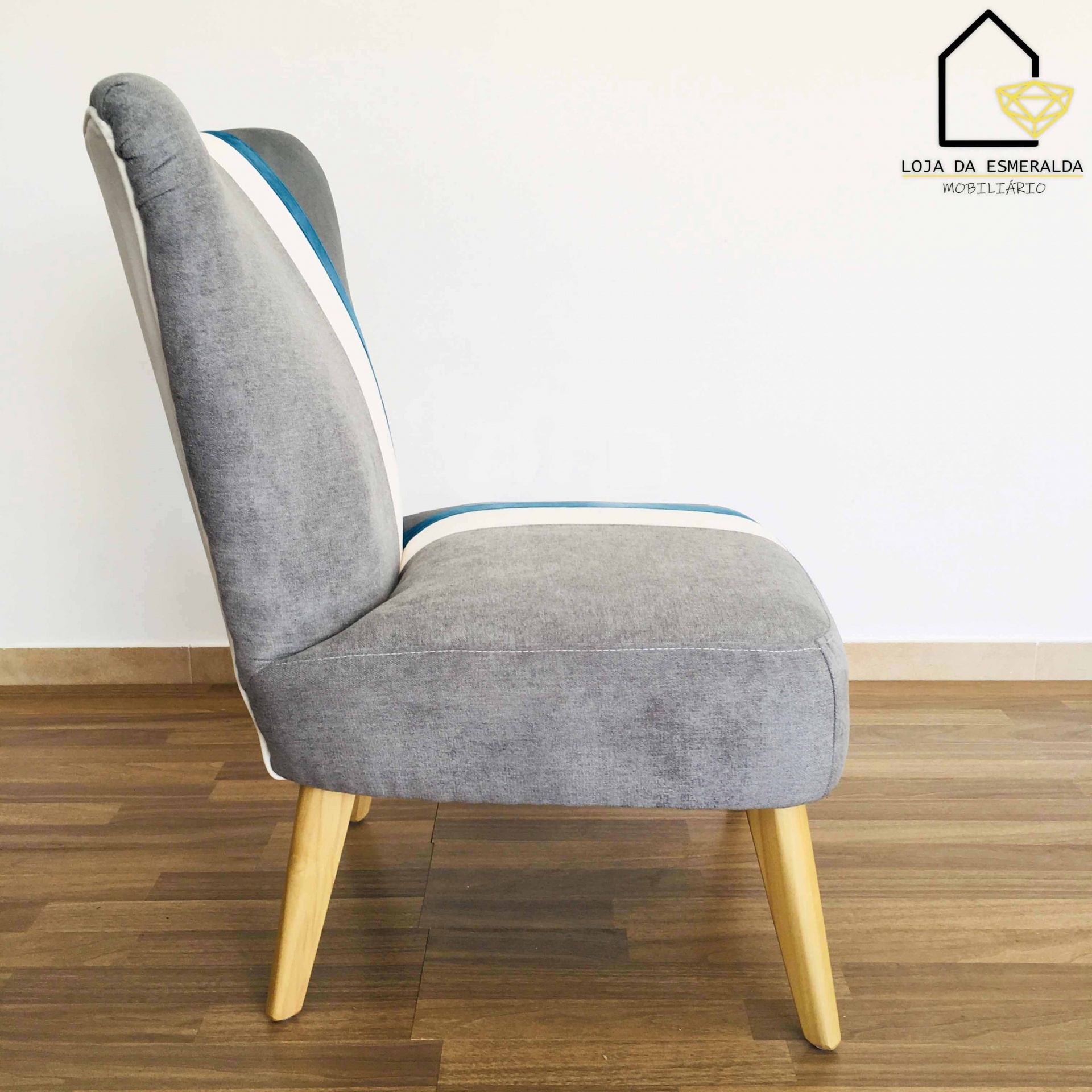 cadeira estofada cinza azul branco com pernas de madeira em chão e parede branca
