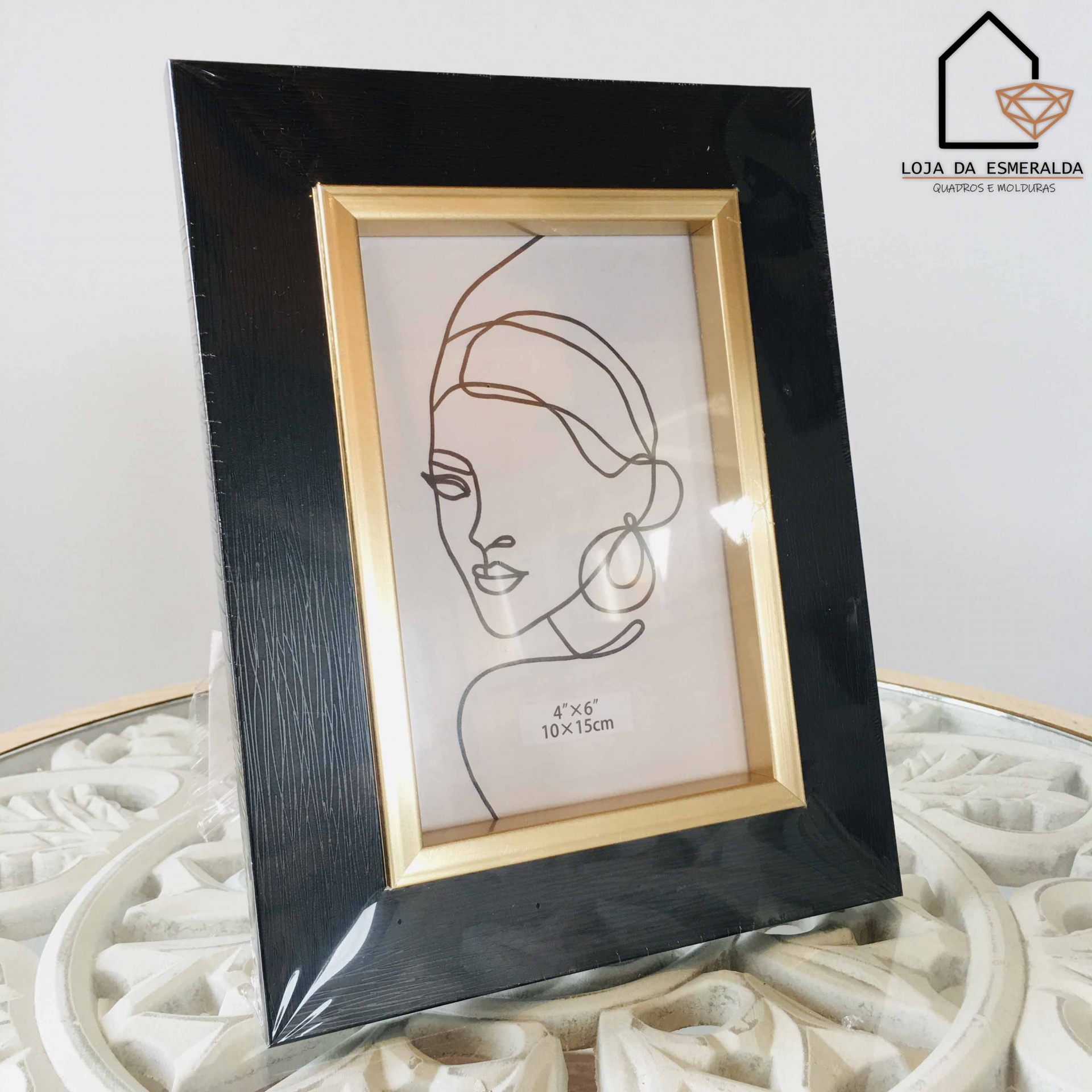 Moldura preta e dourada com desenho minimalista de mulher numa mesa branca decorativa