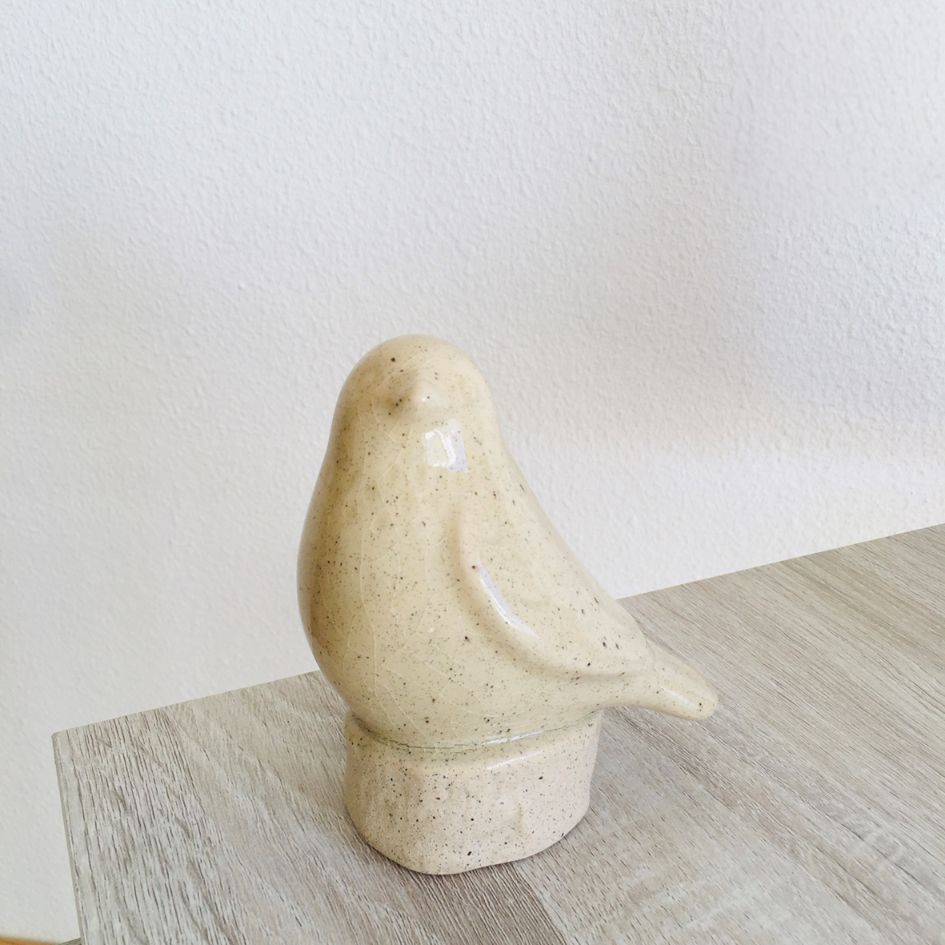 Estatueta de pássaro em cerâmica bege sobre mesa de madeira clara
