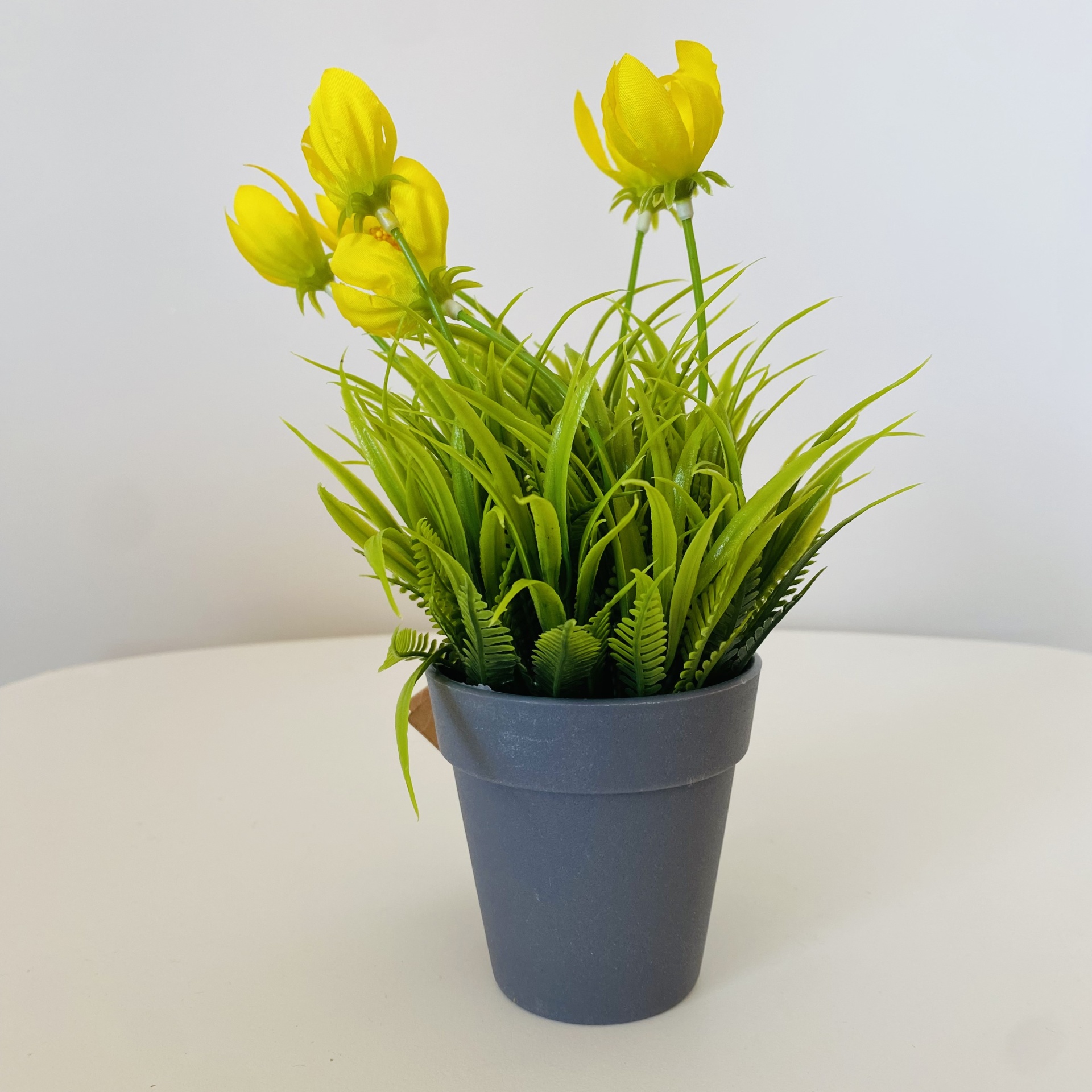 Vaso cinzento com planta artificial de folhas verdes e flores amarelas