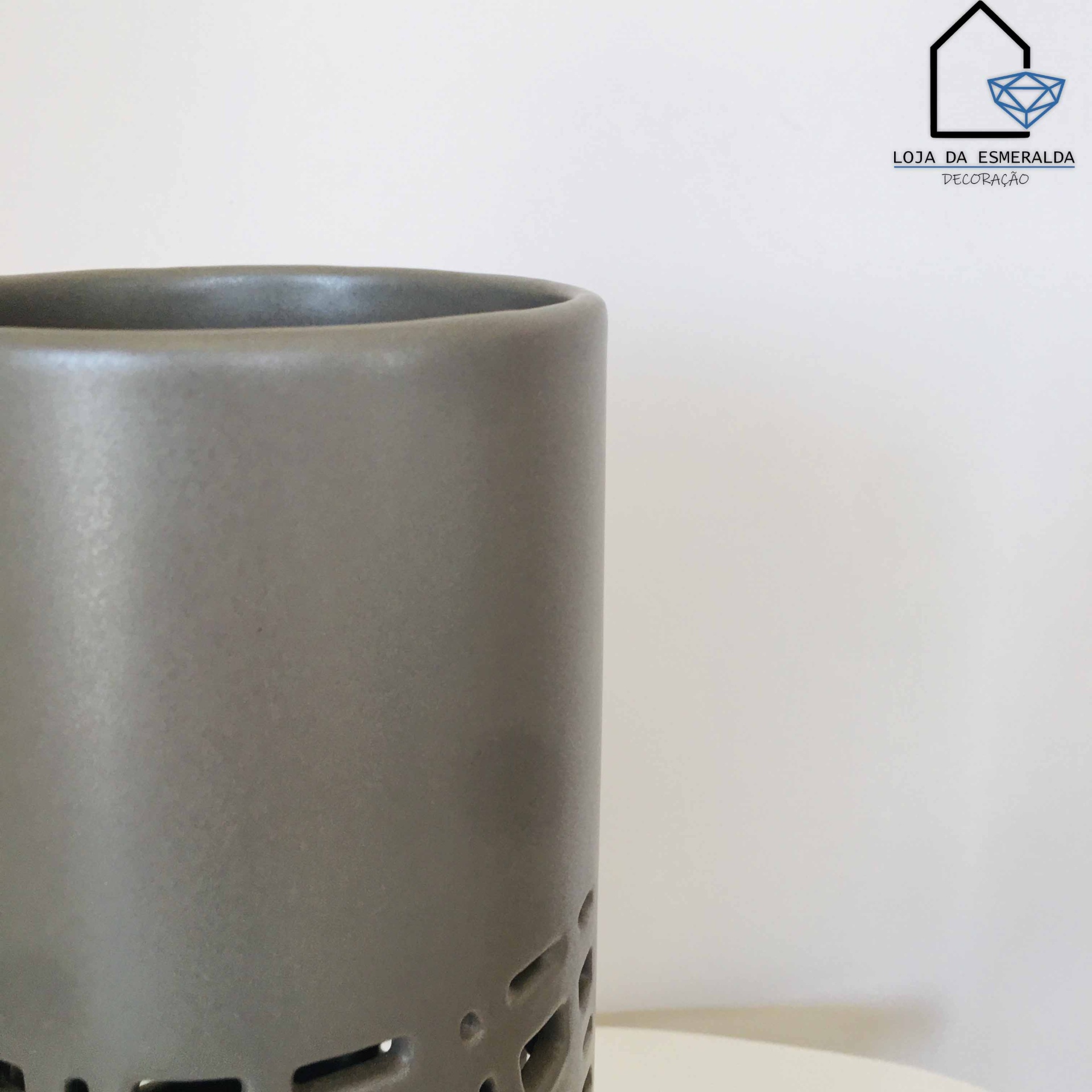 Vaso cilíndrico cinza escuro com recortes geométricos na base sobre superfície branca