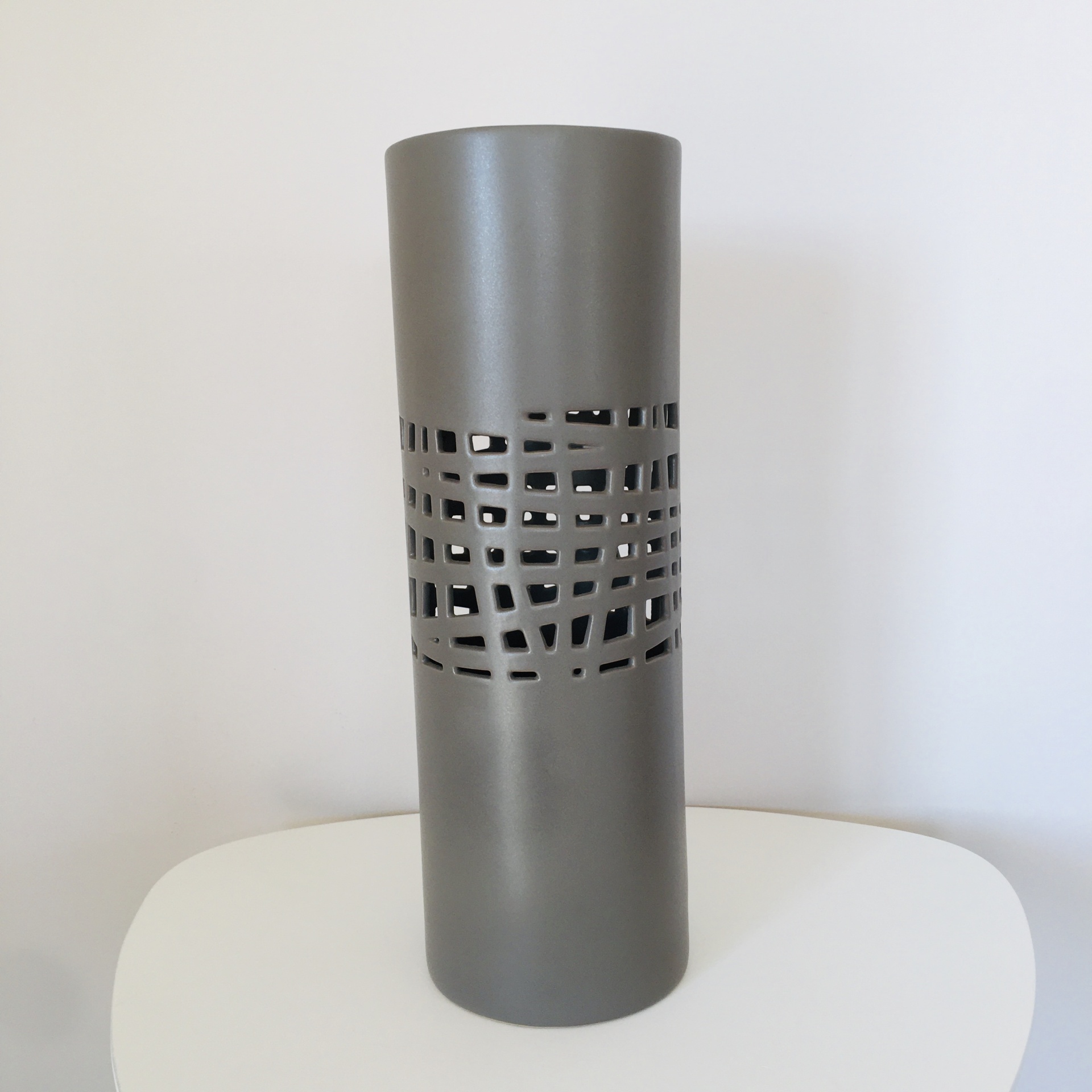 Vaso cilíndrico cinzento com padrões de recortes geométricos