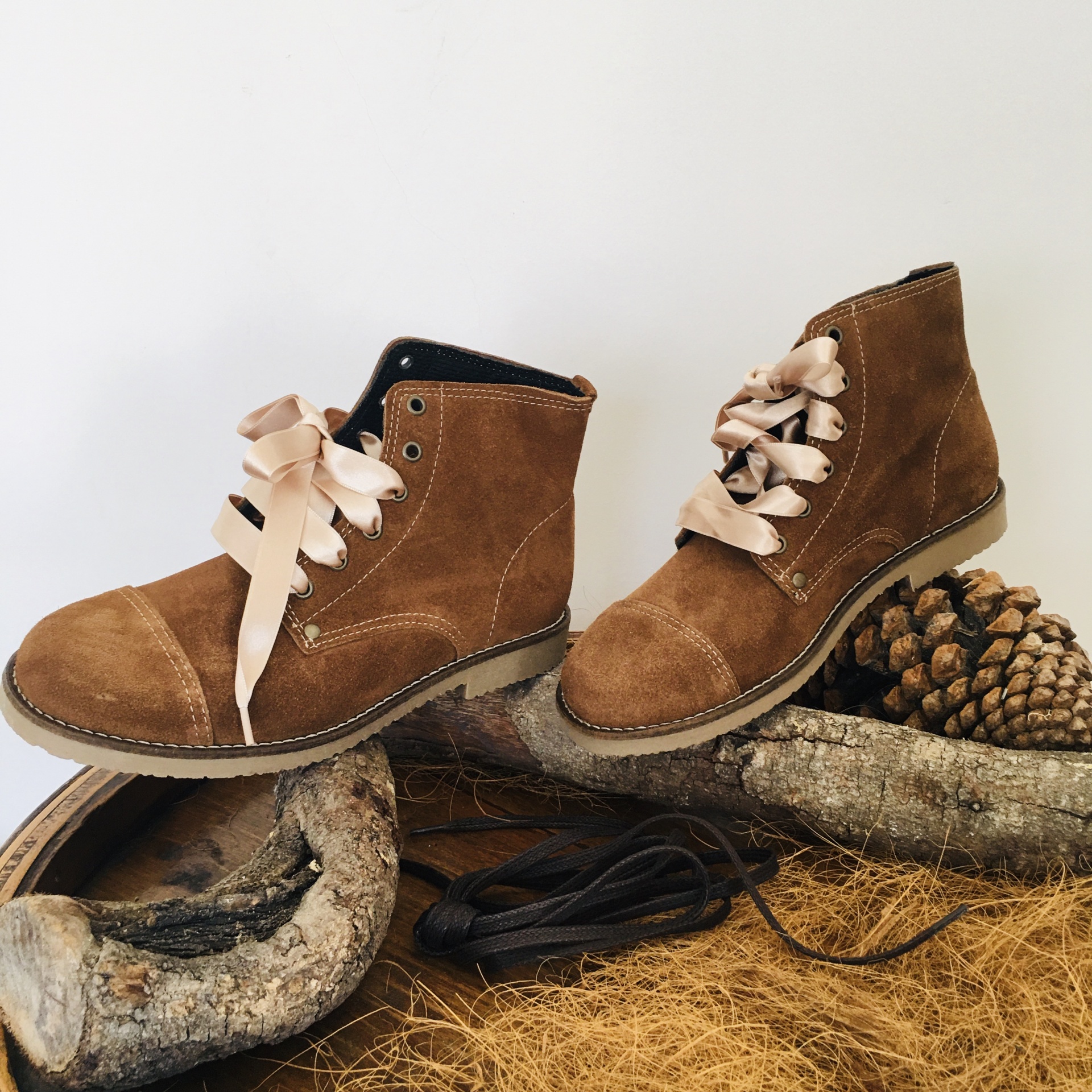 Botas castanhas de camurça com atacadores de fita cor de creme sobre madeira e pinhas