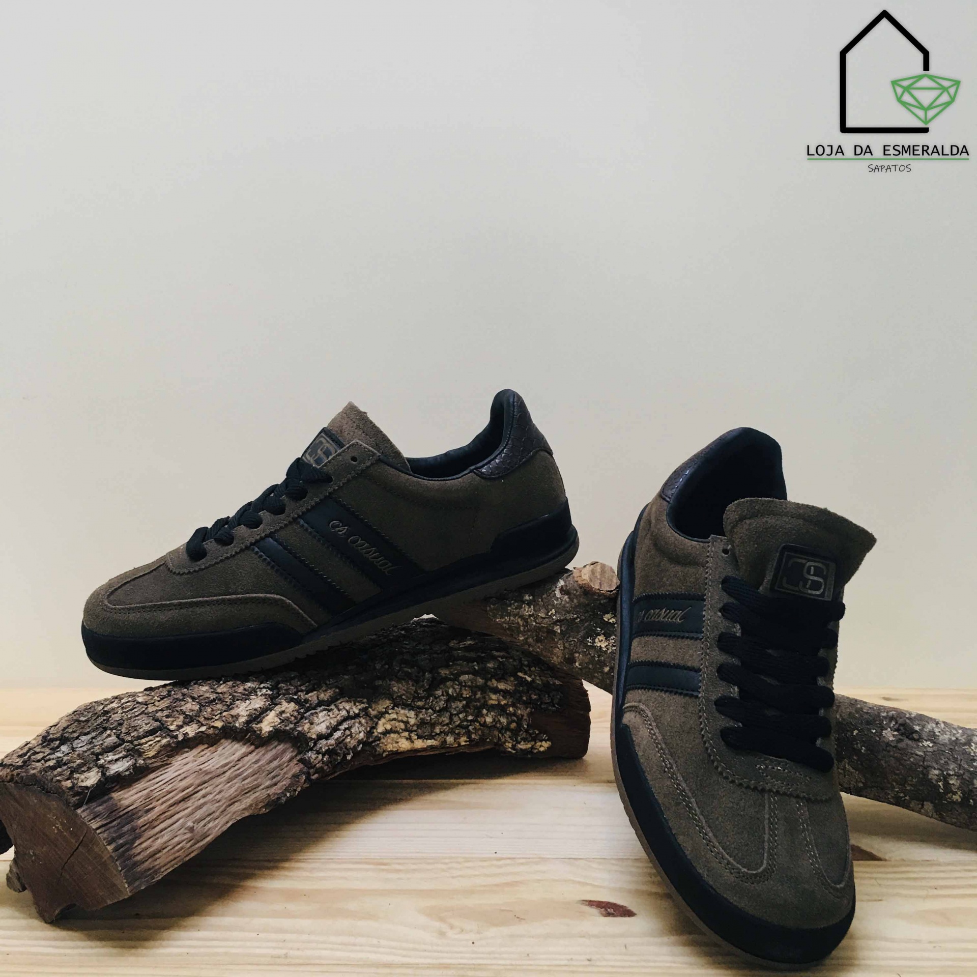 Ténis verde-oliva com detalhes pretos em camurça e tecido sobre troncos de madeira