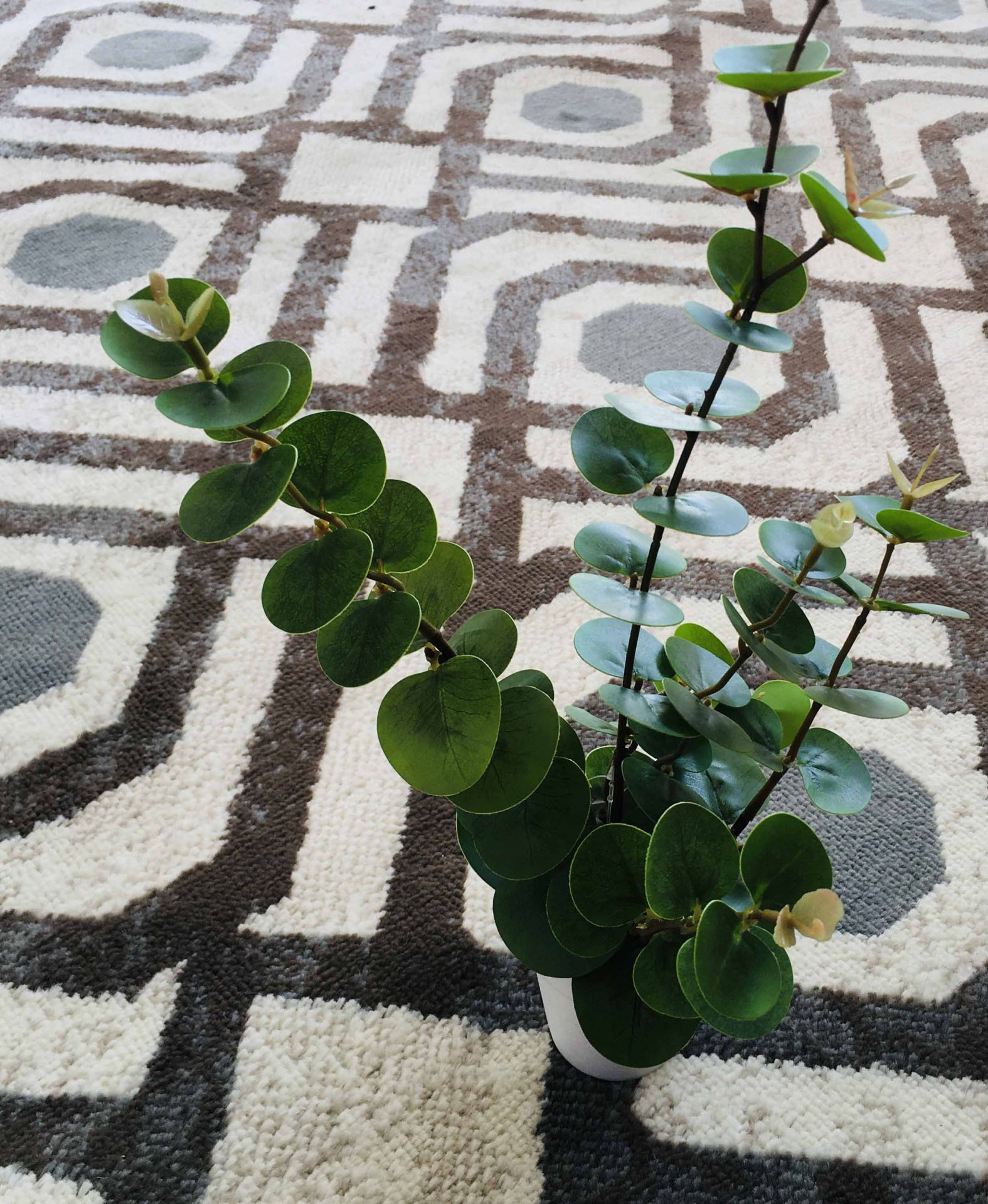 Planta artificial verde num vaso branco sobre tapete com padrão geométrico