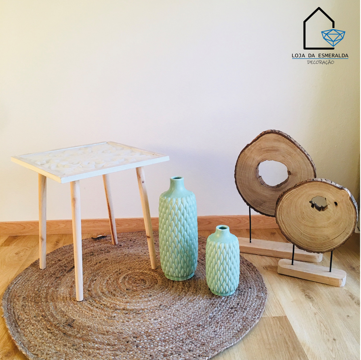 Mesa branca, dois vasos verdes texturizados, fatias de madeira em suportes num tapete redondo.
