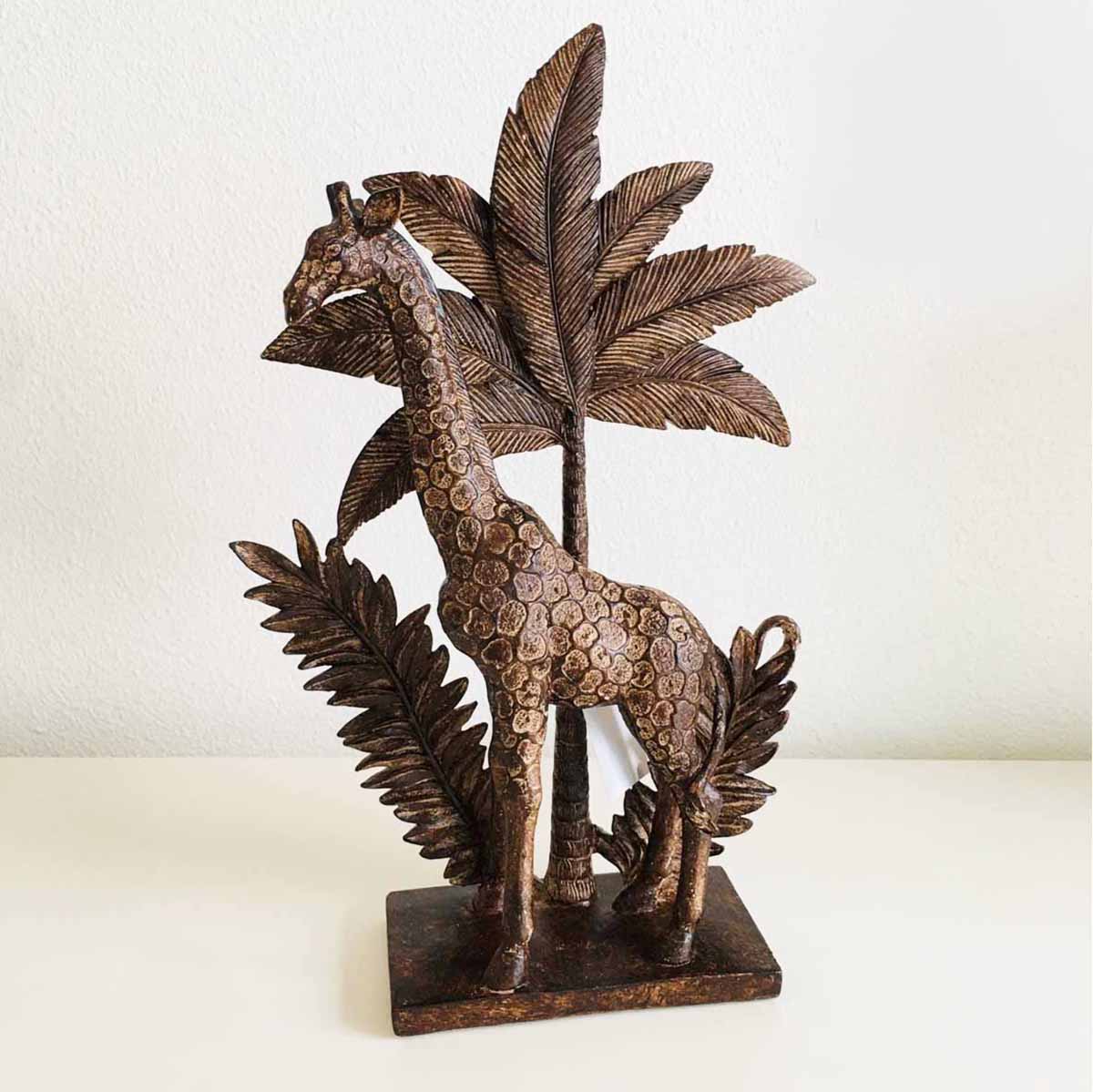 Estátua decorativa de girafa marrom com folhas ao fundo