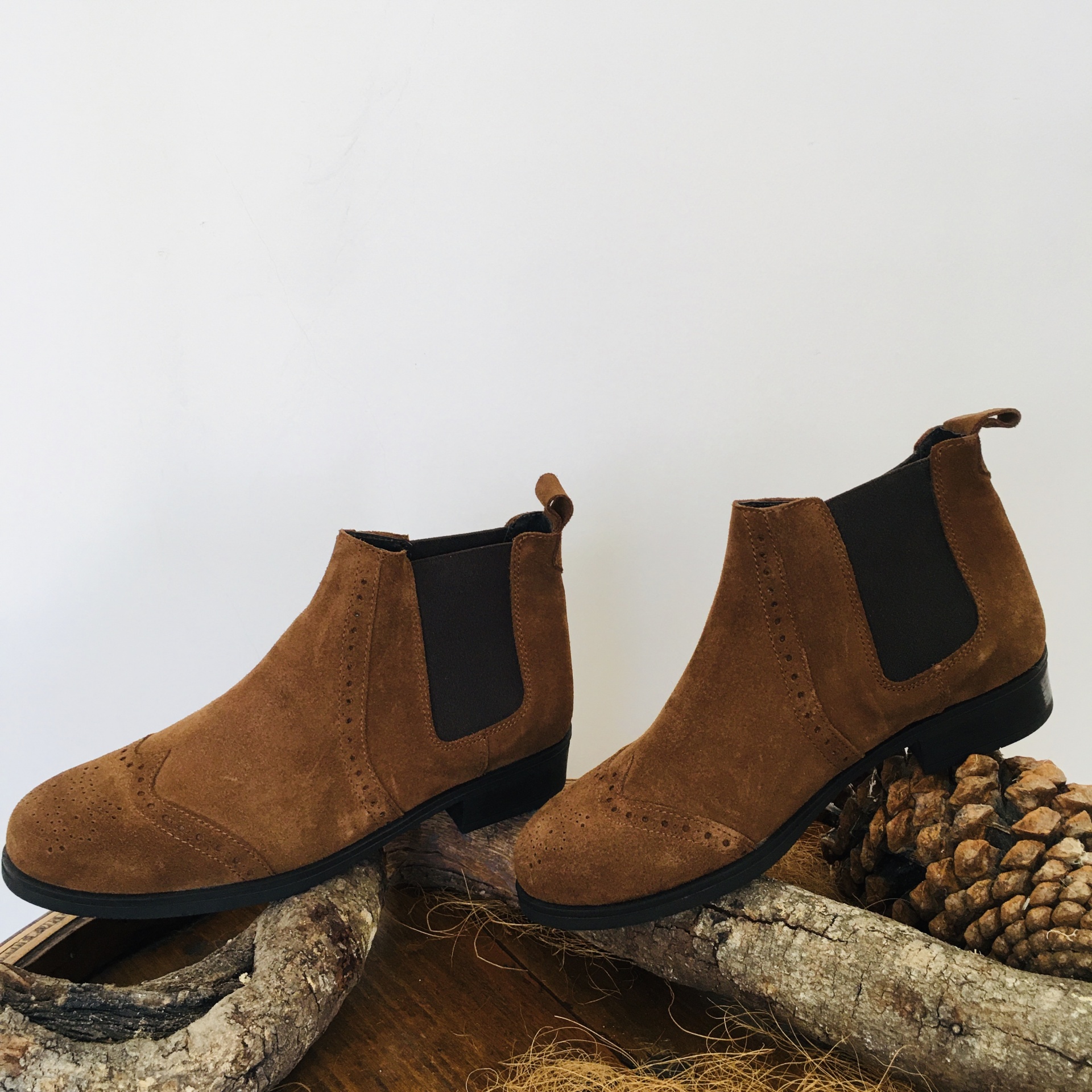 Botas Chelsea castanhas em camurça com elásticos pretos sobre tronco com pinhas