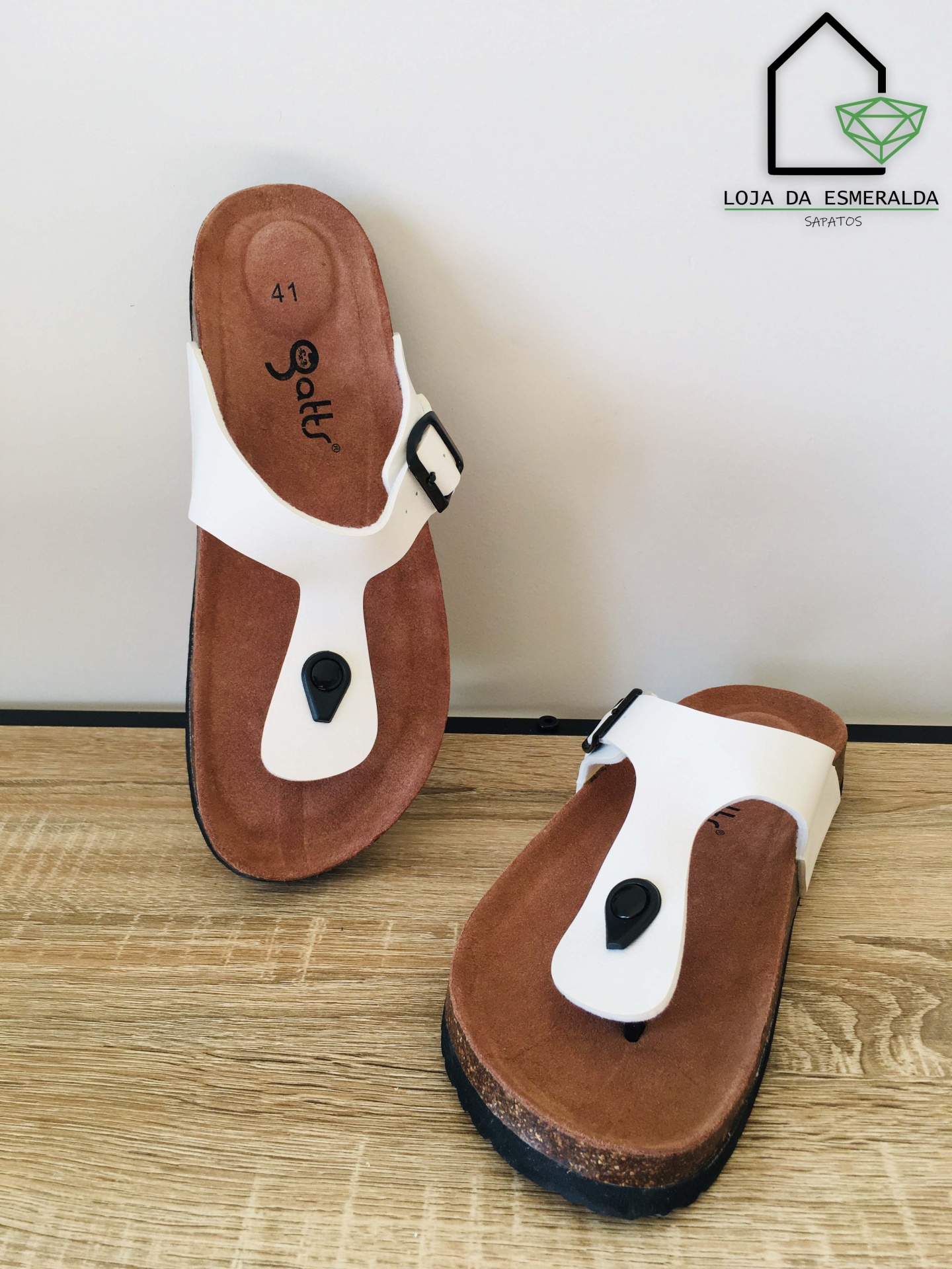 Chinelos de dedo brancos com palmilha castanha e detalhe preto sobre madeira clara