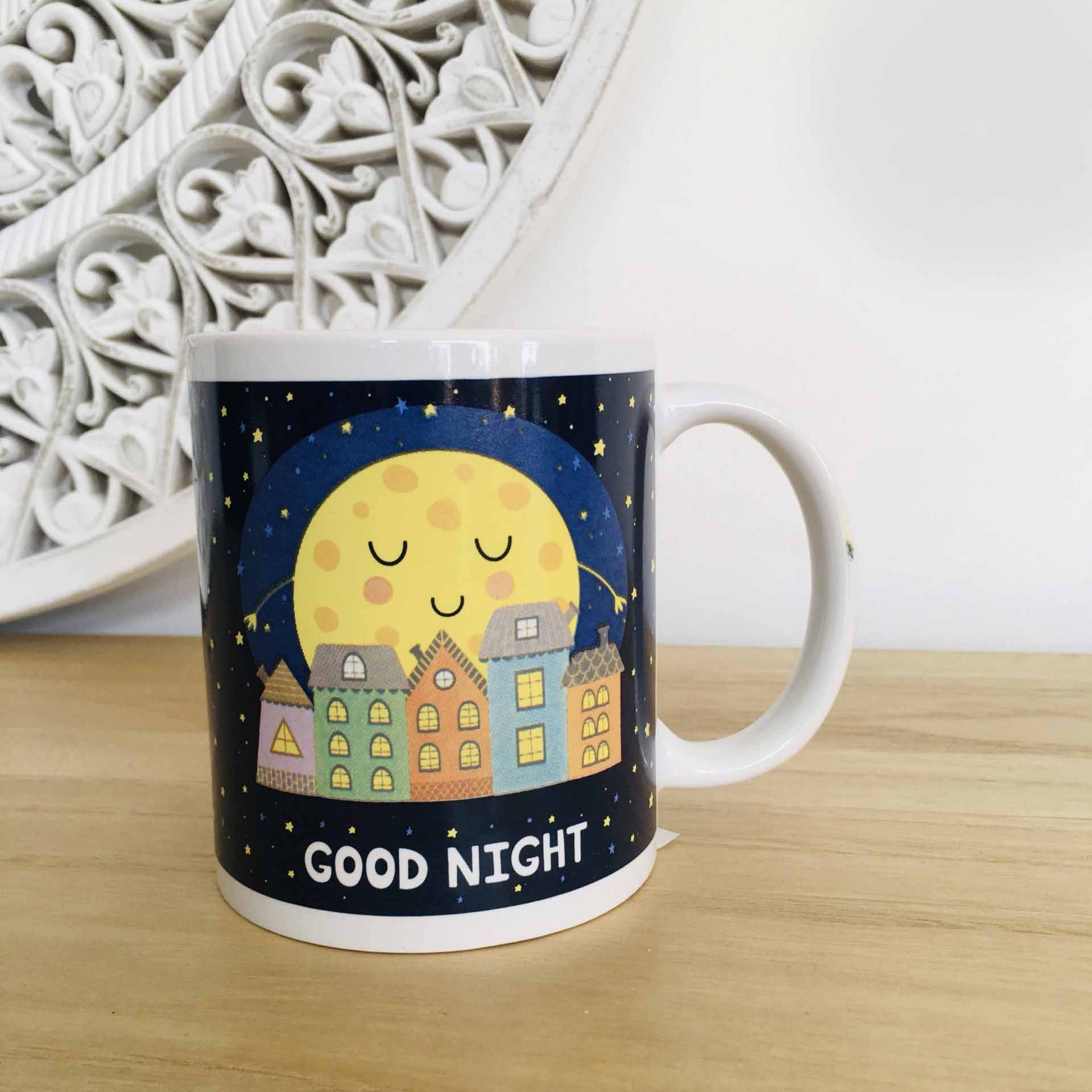 Caneca branca com design de lua sorridente, casas coloridas e texto GOOD NIGHT