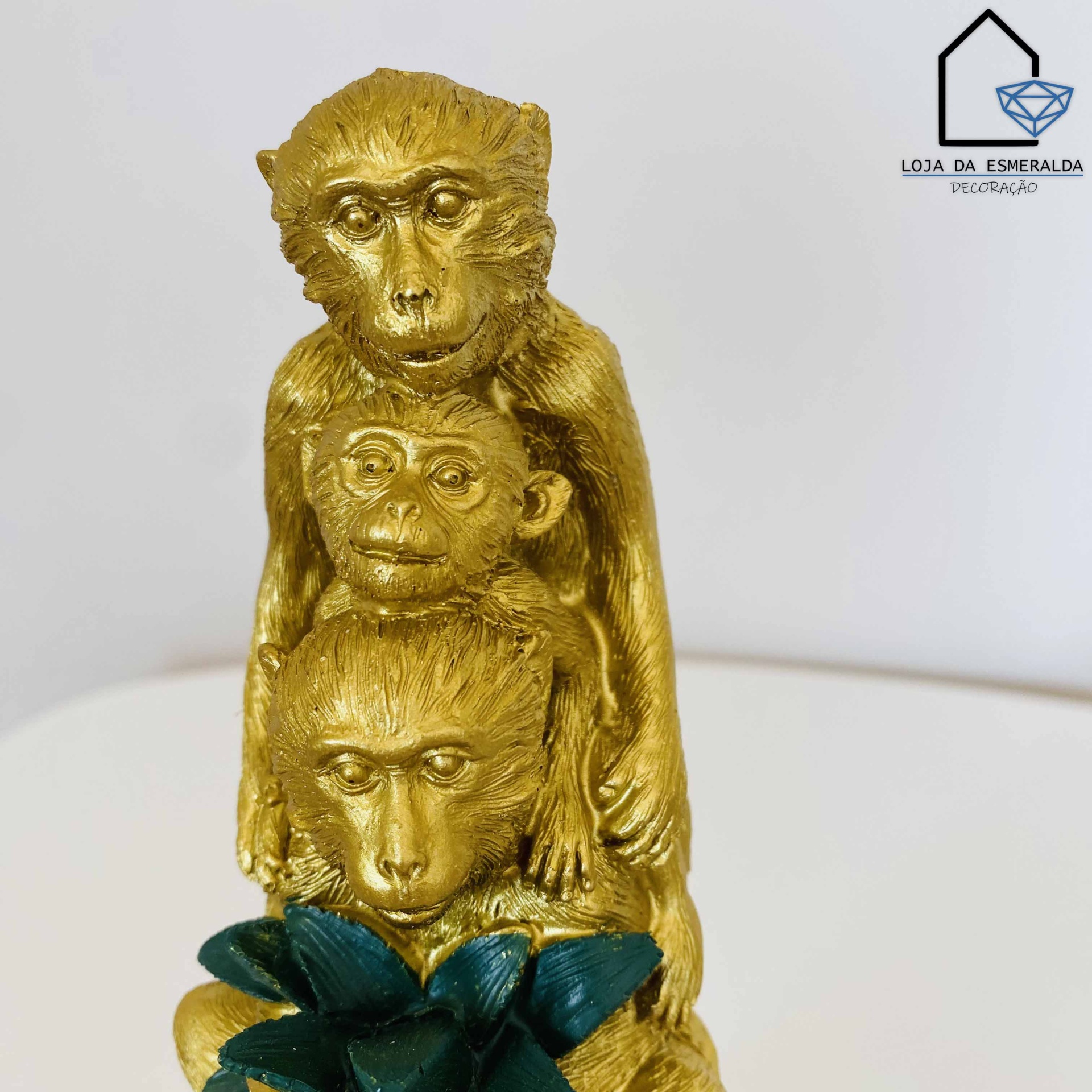 Escultura dourada de três macacos empilhados com folhas verdes