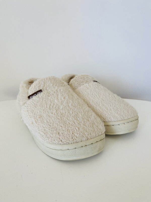 Chinelos felpudos bege claro com sola branca sobre superfície branca