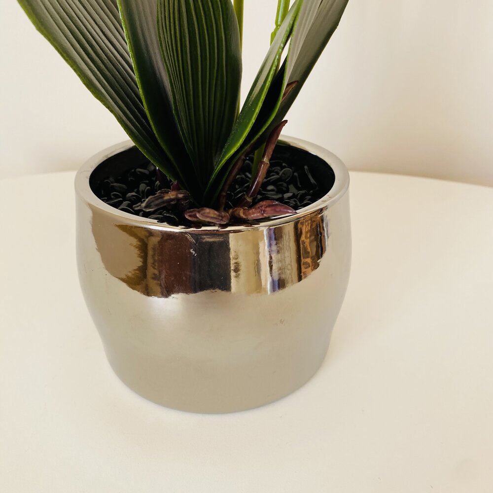 Vaso cerâmico prateado com planta artificial verde sobre superfície branca