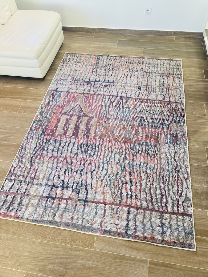 Tapete colorido abstrato sobre chão de madeira ao lado de sofá creme