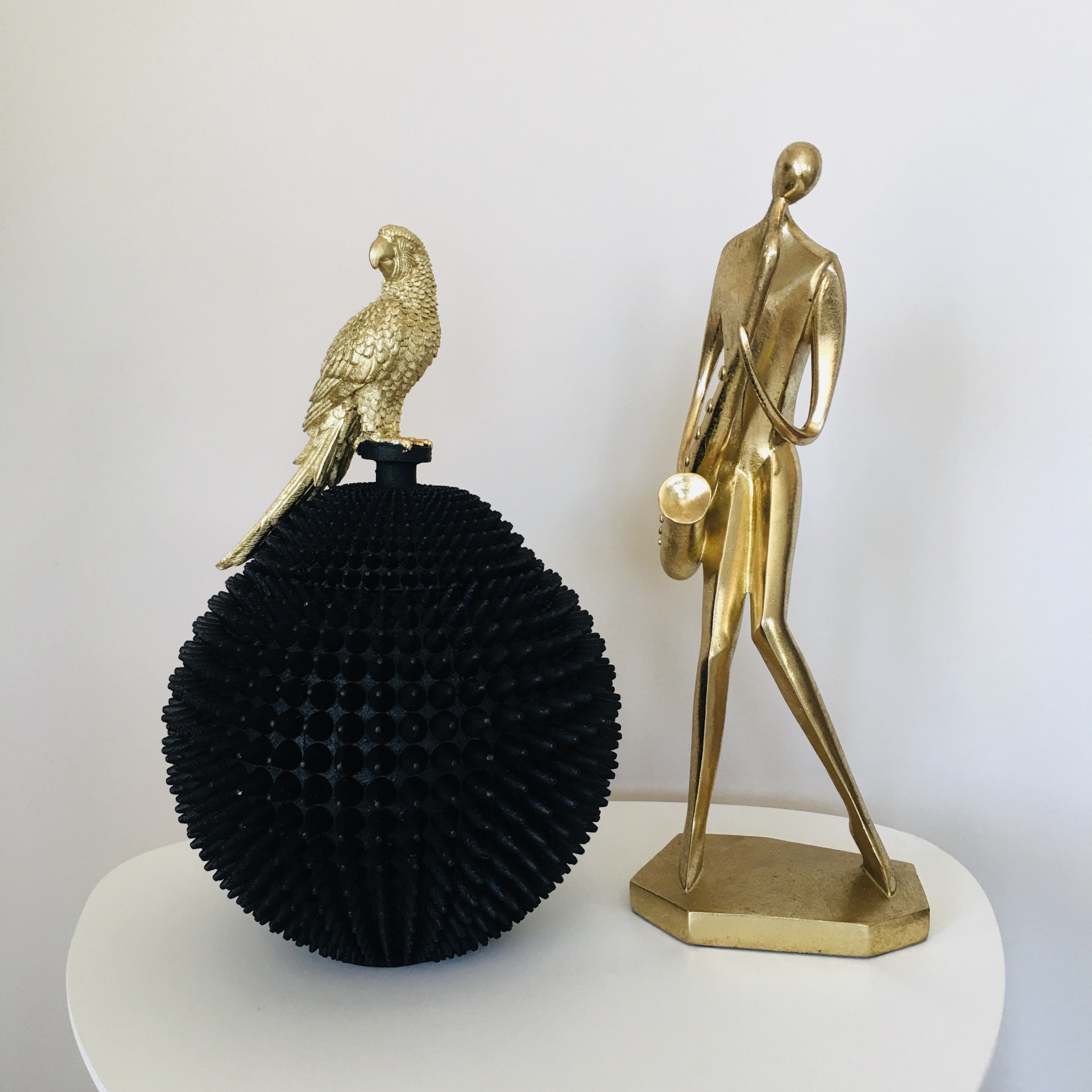 Objeto decorativo preto com pássaro dourado e estátua dourada de figura humana com saxofone
