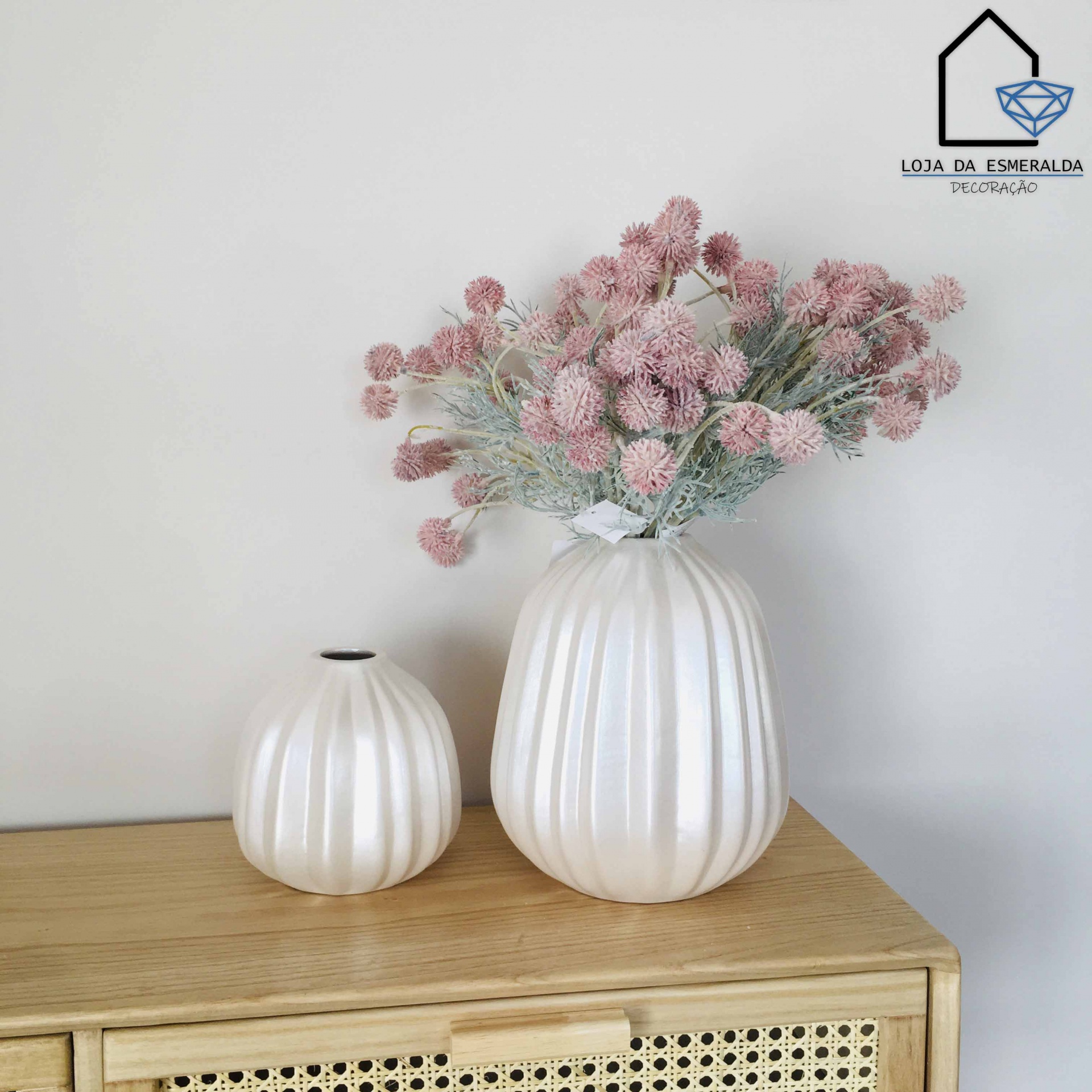 Dois jarros cerâmicos brancos com flores artificiais cor-de-rosa sobre móvel de madeira clara