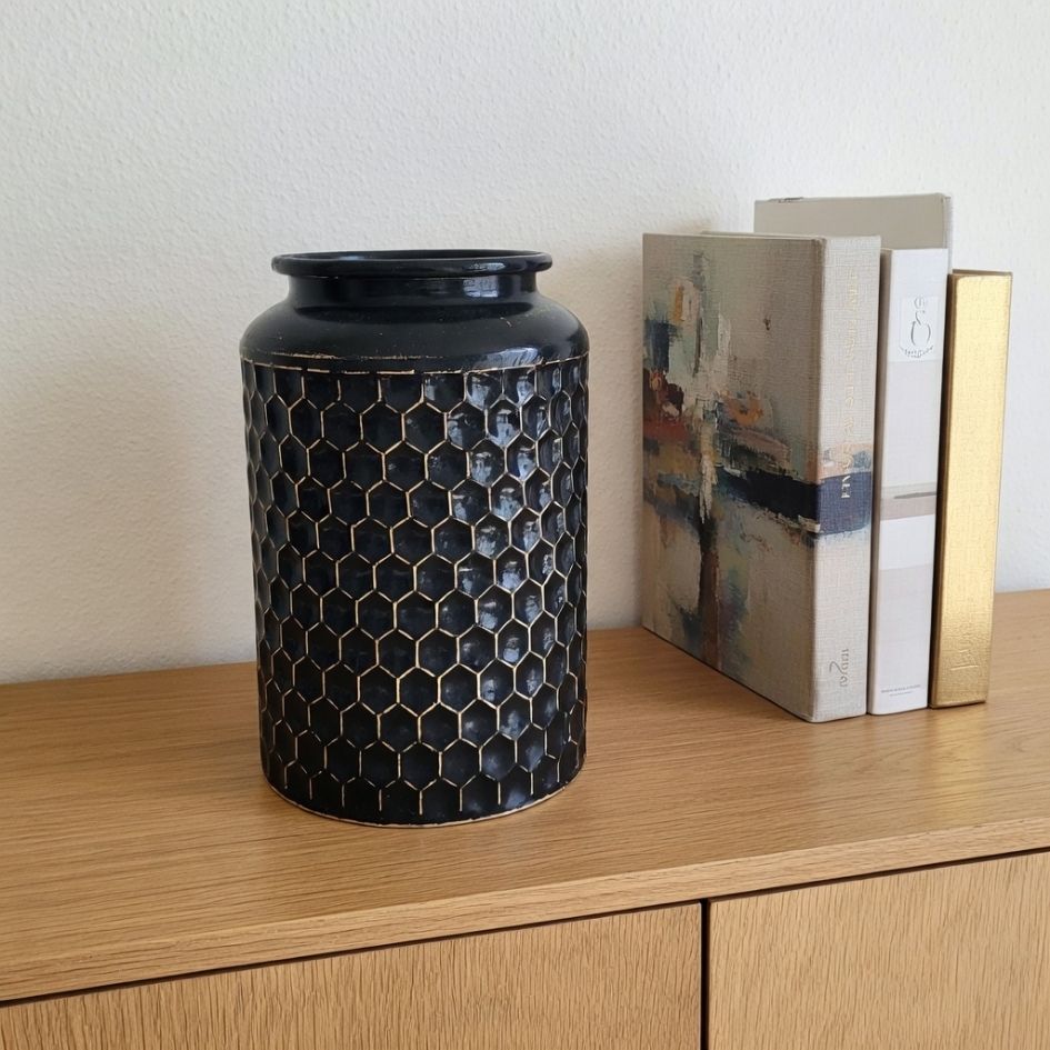 Vaso de cerâmica preto com padrão hexagonal dourado e livros ao lado numa superfície de madeira.