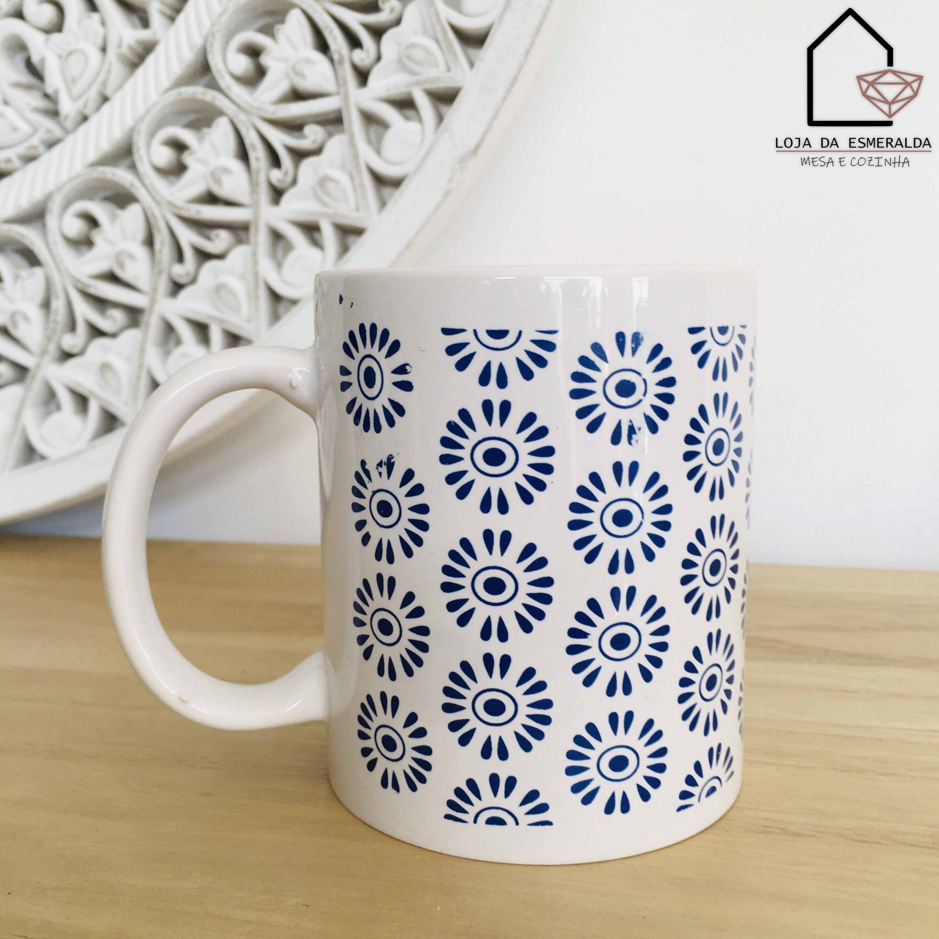 Caneca branca com padrão azul de flores estilizadas sobre mesa de madeira clara