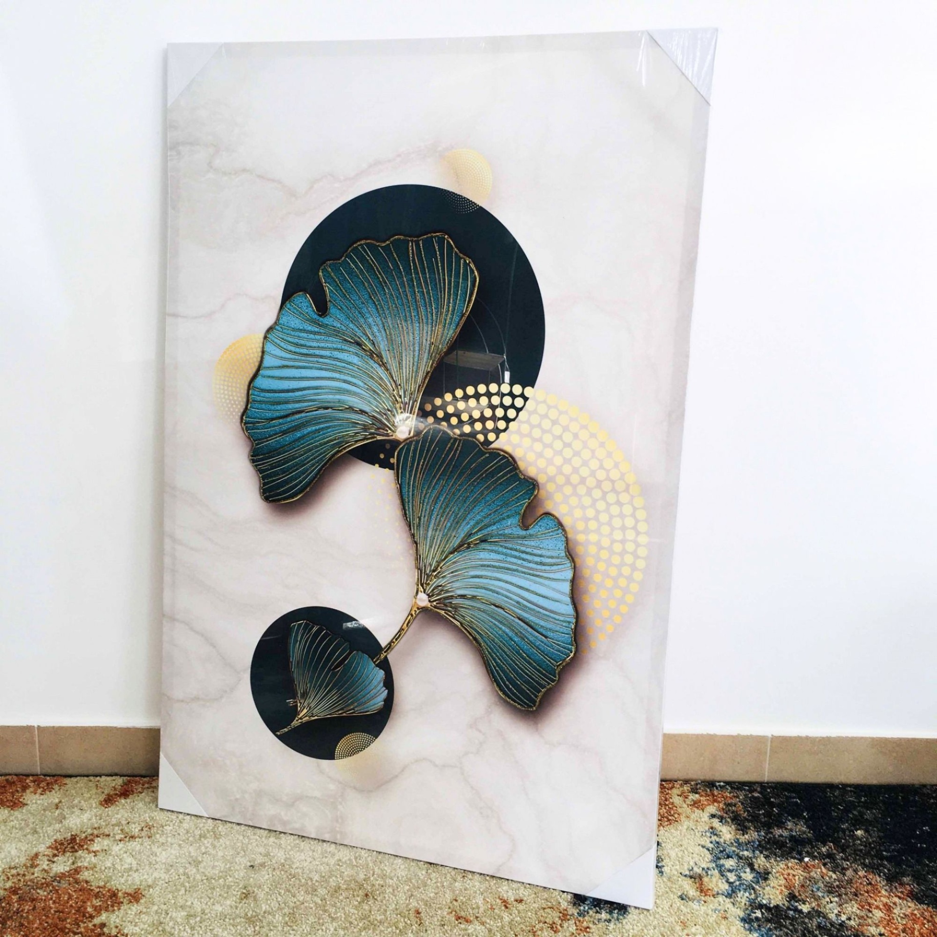 Quadro decorativo com folhas azul e dourado sobre círculos pretos e dourados em fundo de mármore branco