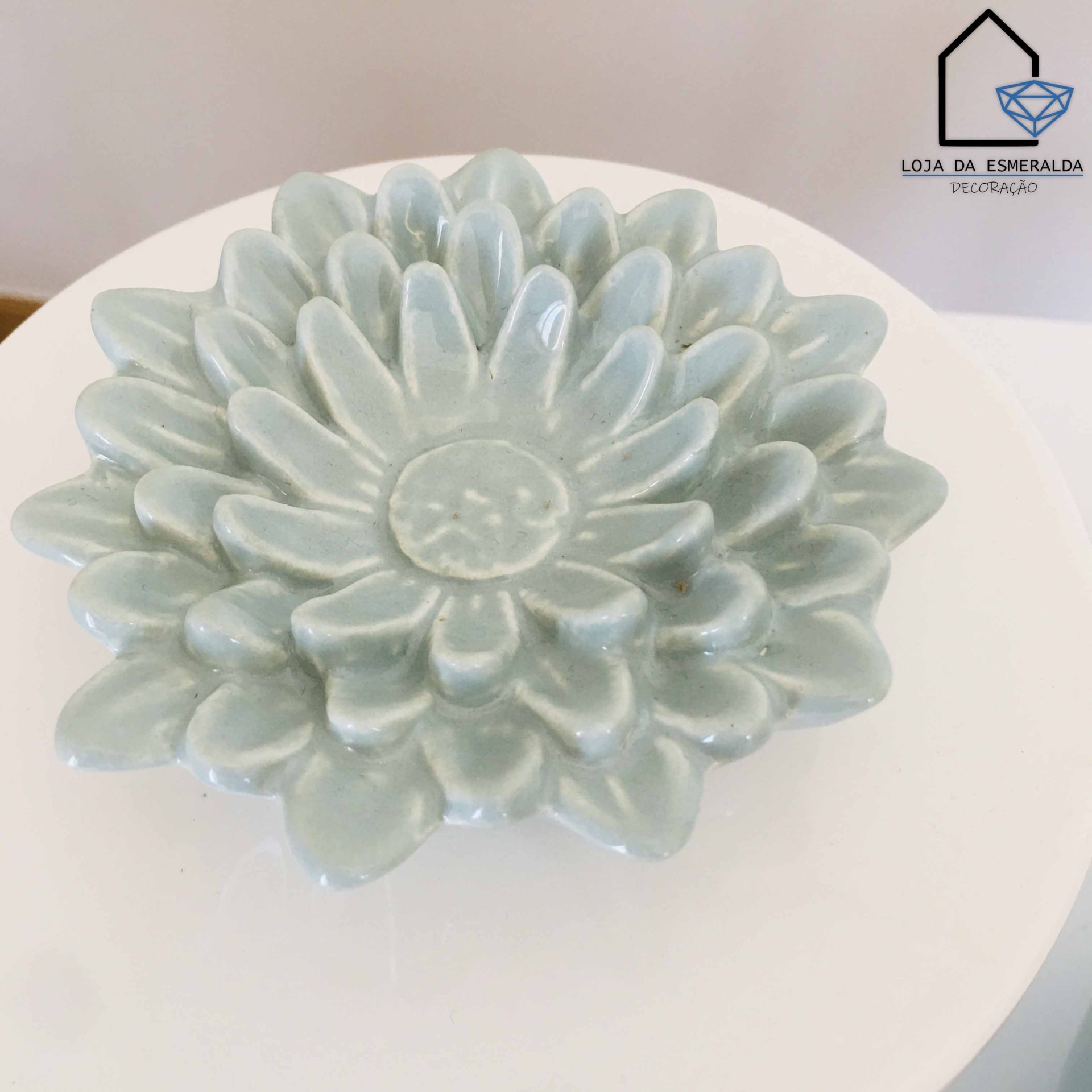 Prato decorativo verde água em forma de flor em superfície branca.