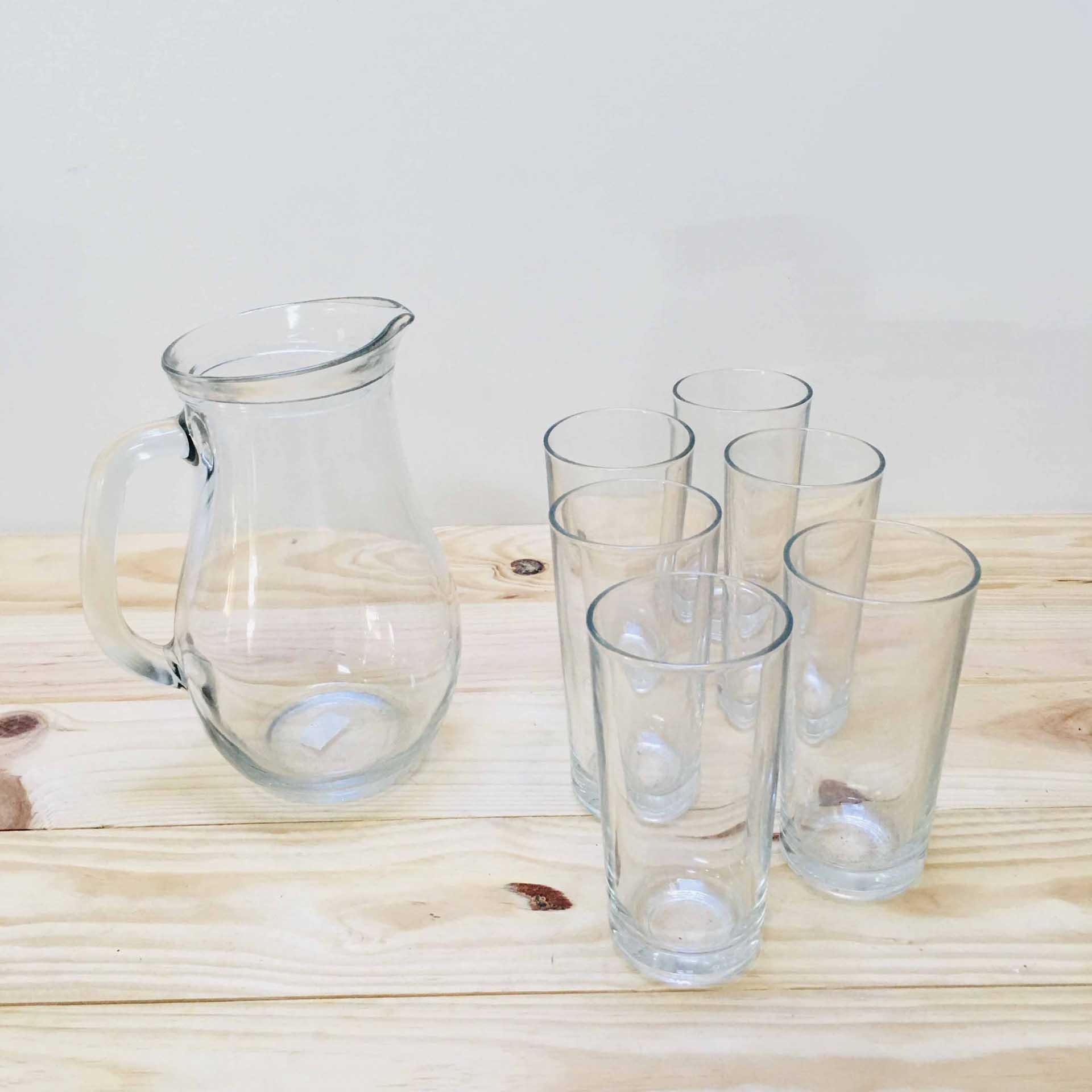 Jarra e cinco copos altos transparentes em vidro num tampo de madeira clara