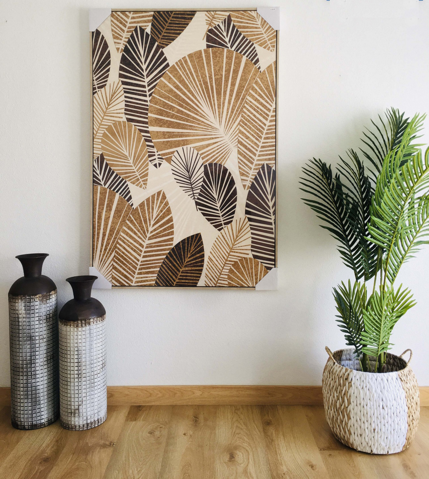 Quadro decorativo de folhas castanhas e pretas com vasos e planta num chão de madeira clara.