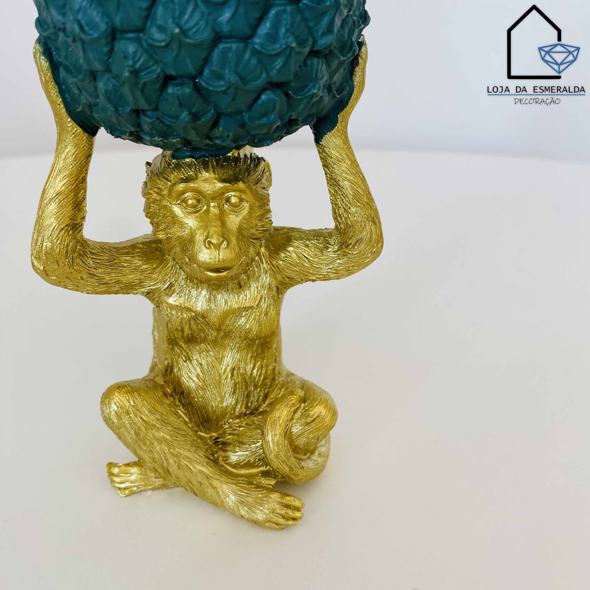 Escultura de macaco dourado segurando esfera verde texturizada