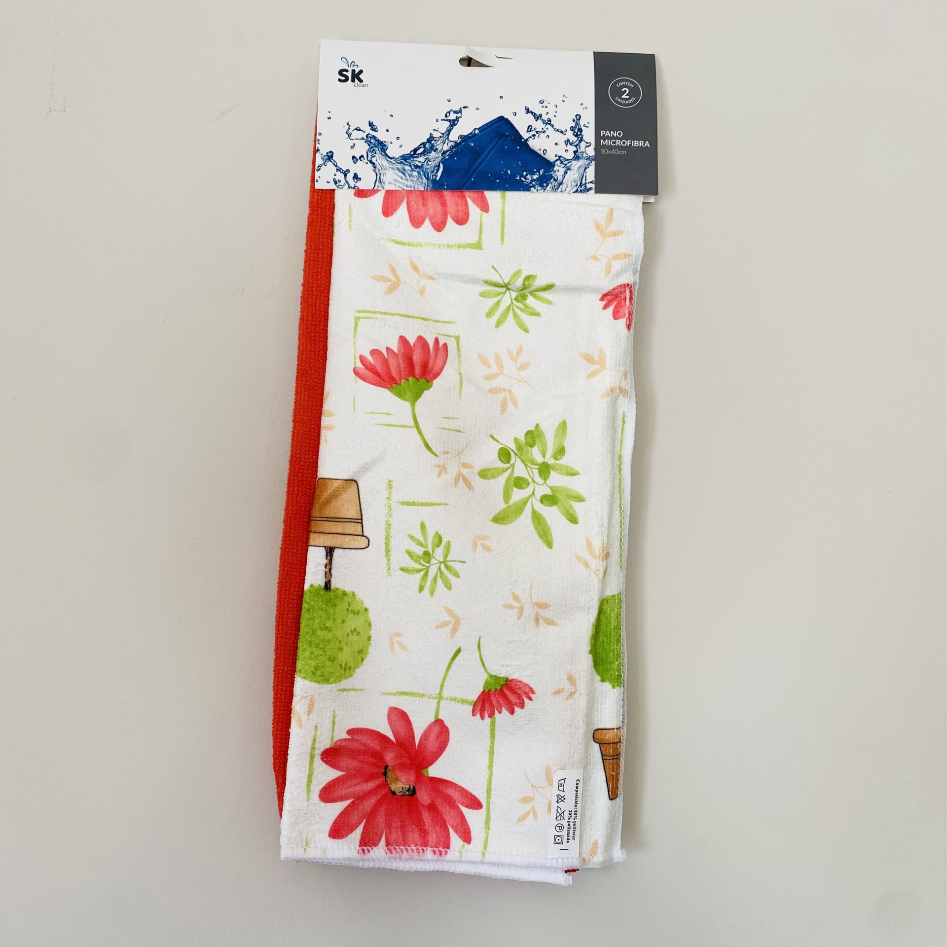 Dois panos de cozinha, um branco com flores vermelhas e outro vermelho liso, embalados