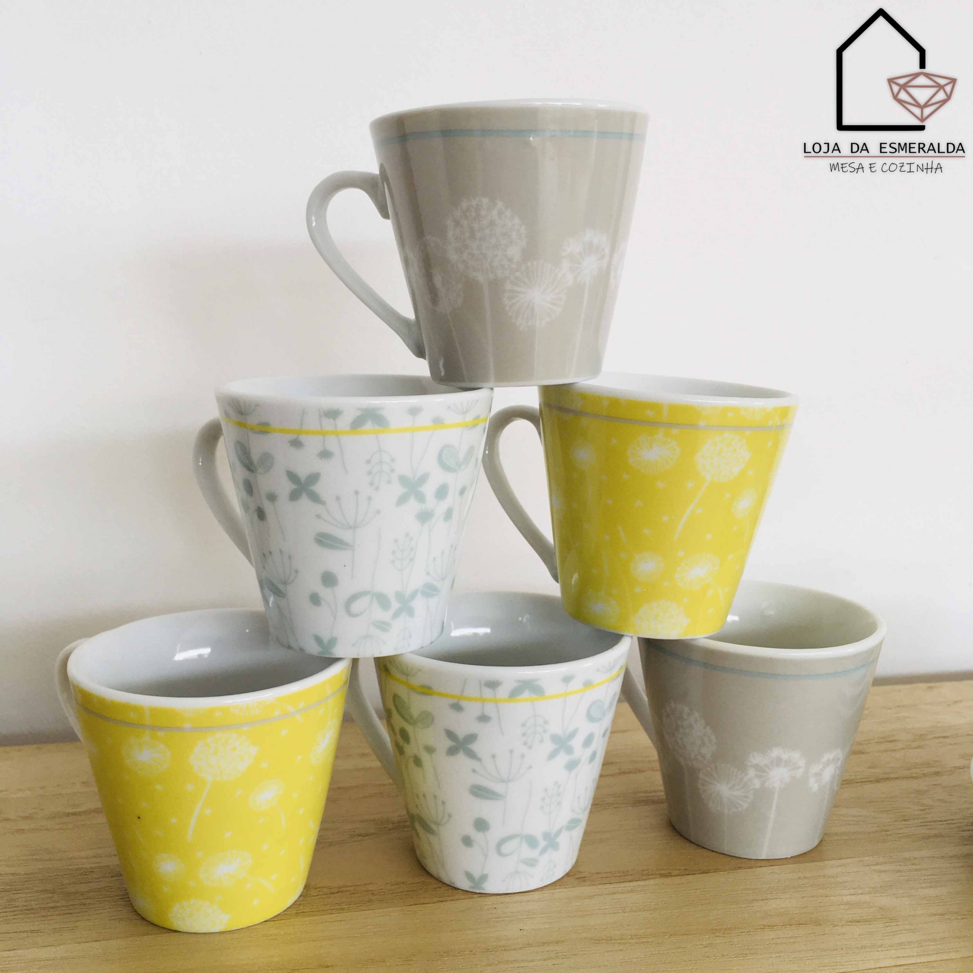 Seis canecas de cerâmica coloridas com padrões florais empilhadas sobre mesa de madeira