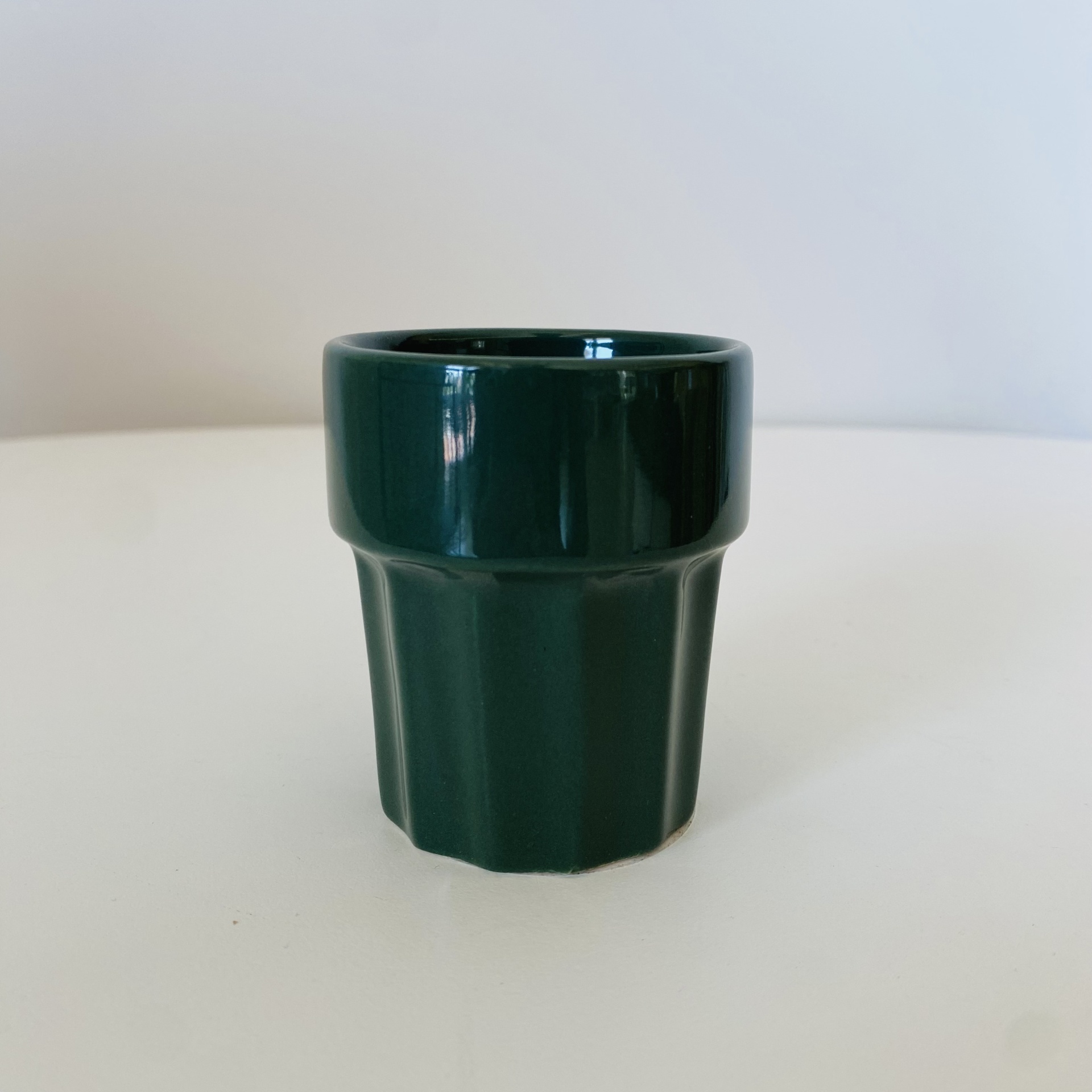 Copo pequeno de cerâmica verde escuro com relevo em superfície branca